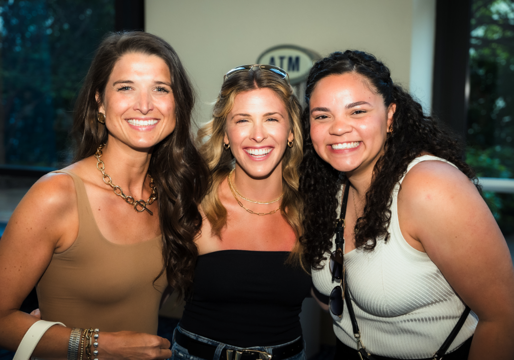 Three women smiling and posing together indoors.