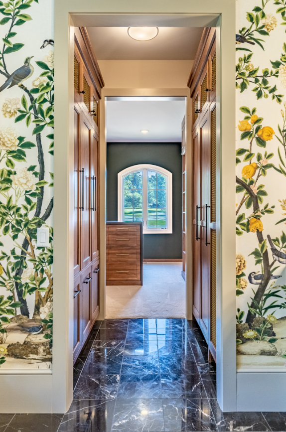 View through doorway into room with window and wooden cabinetry, wallpaper with birds and flowers, and marble flooring.