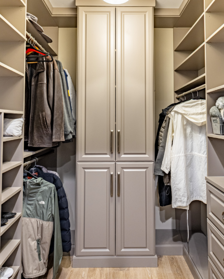 Walk-in closet with shelves and hanging clothes on both sides and a tall white cabinet in the center.