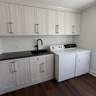 Laundry room with white cabinets, black countertop, black faucet, and a white washing machine and dryer.