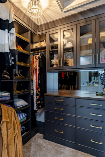 A walk-in closet with built-in cabinets, shelves, and drawers filled with clothing, accessories, and shoes, with a chandelier overhead.