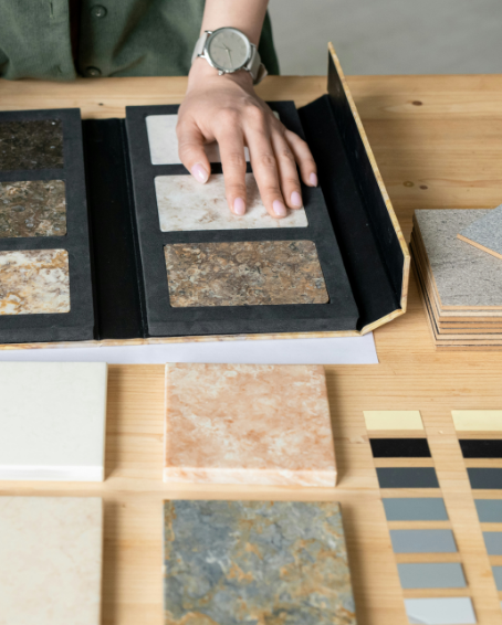 Person examining a sample book of various stone and tile materials on a wooden table.