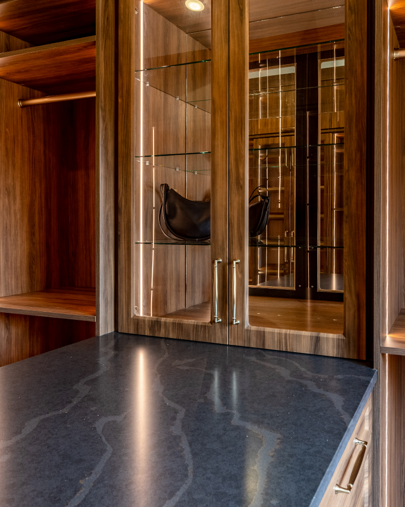 Wooden display cabinet with glass doors and shelves, holding a black leather handbag inside.