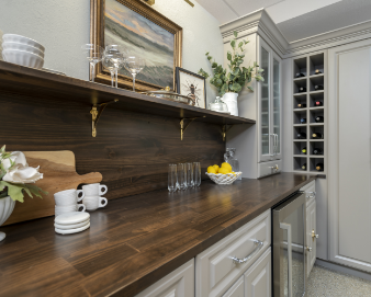 Kitchen counter with glassware, a bowl of lemons, and decorative items, with cabinetry and a wine rack in the background.