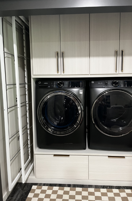 Front view of a black washing machine and dryer side by side in a laundry room with white cabinets above.