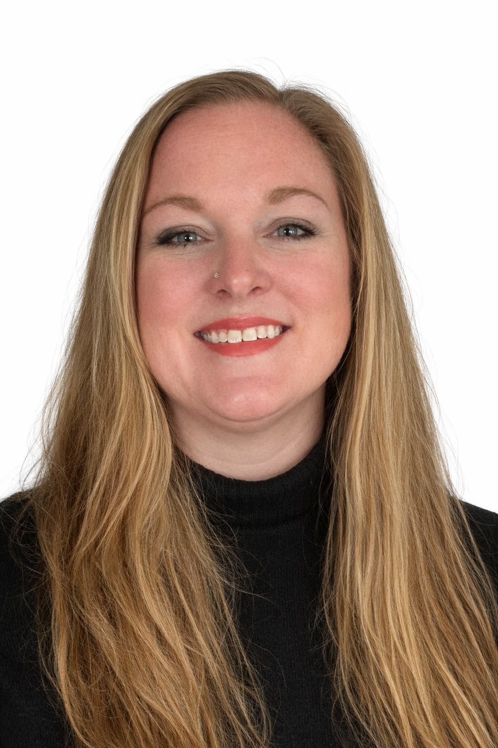 A woman with long blonde hair wearing a black turtleneck, smiling against a white background.