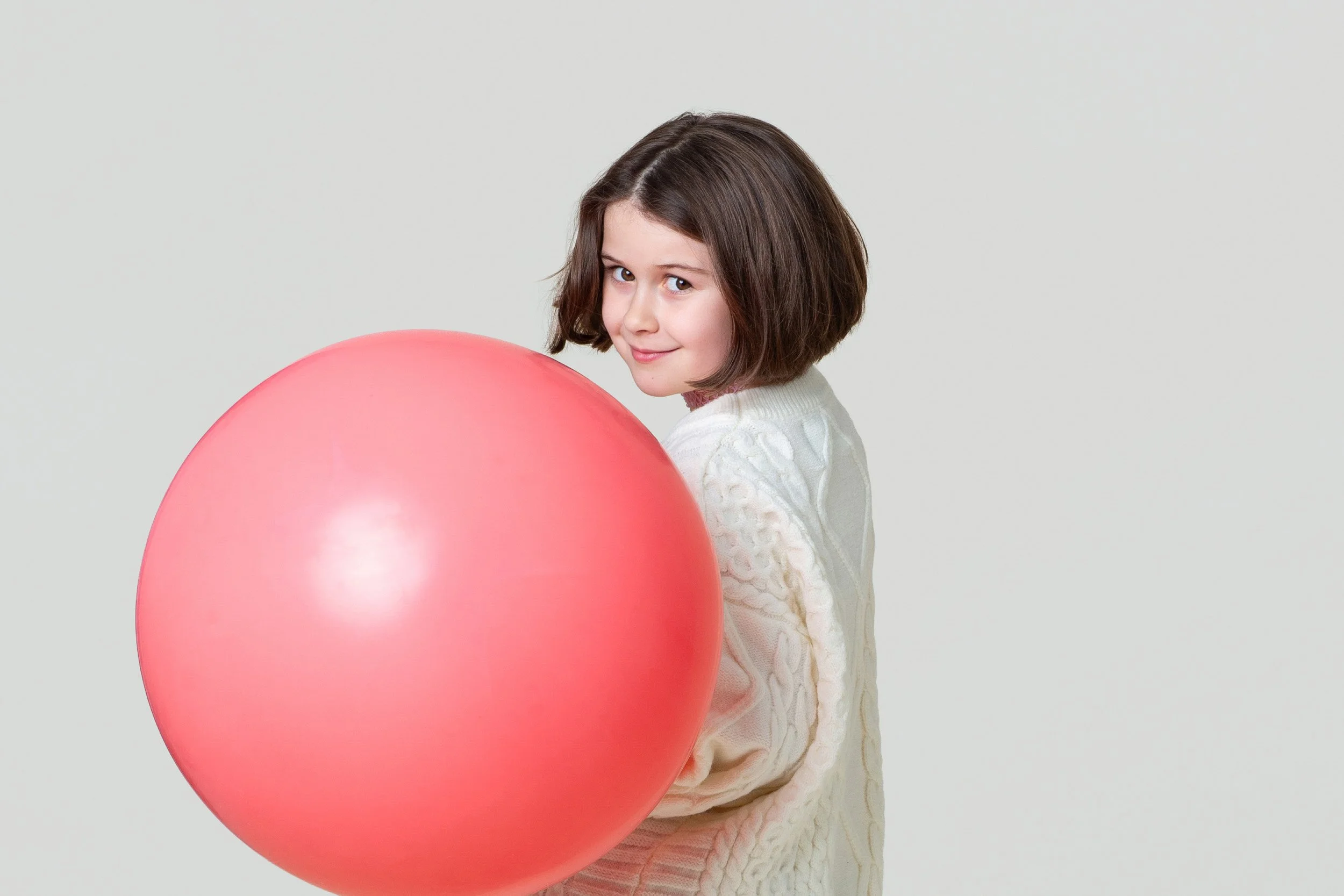 Profile view of a smiling girl holding a large pink balloon during a kids birthday portraits session at Poppie Portraits in Madrona, Seattle.  