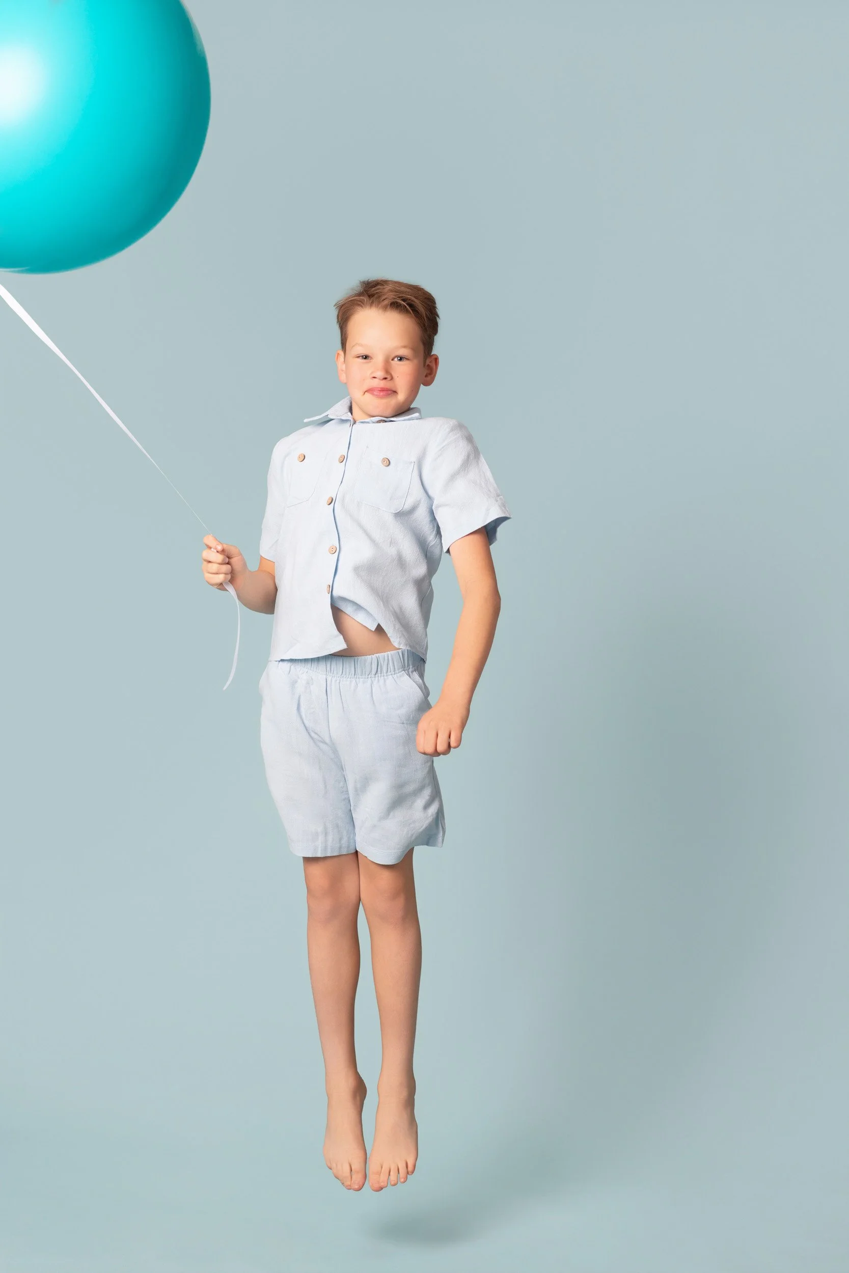 Boy in a matching blue set jumping while wearing a party hat, hands in his pockets during a birthday photoshoot at Poppie Portraits in Seattle. 