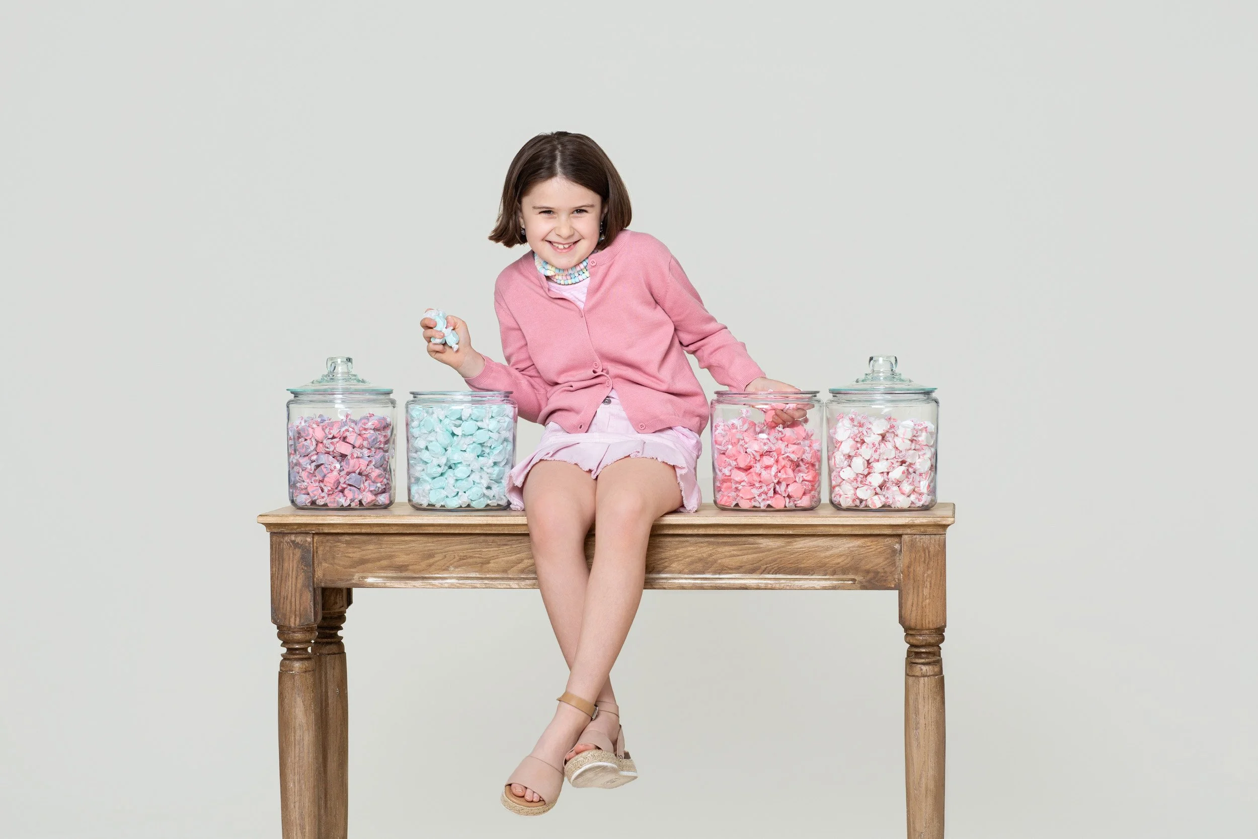 Girl seated on a wooden table lined with jars of pastel candy