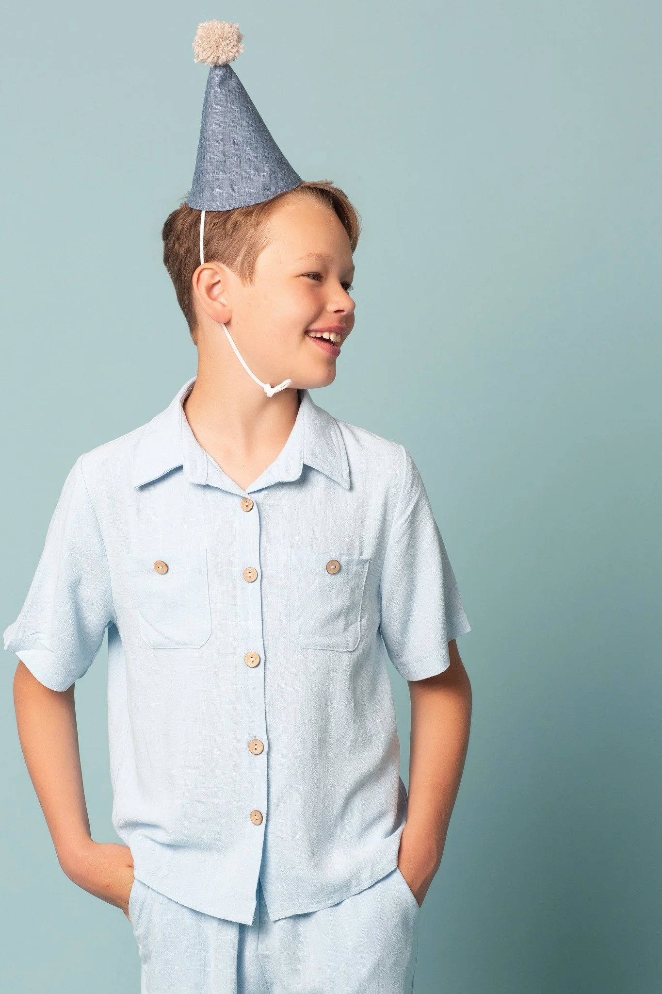 A smiling boy wearing a party hat against an aqua background tint during a kids birthday portraits session at Poppie Portraits in Madrona, Seattle.  