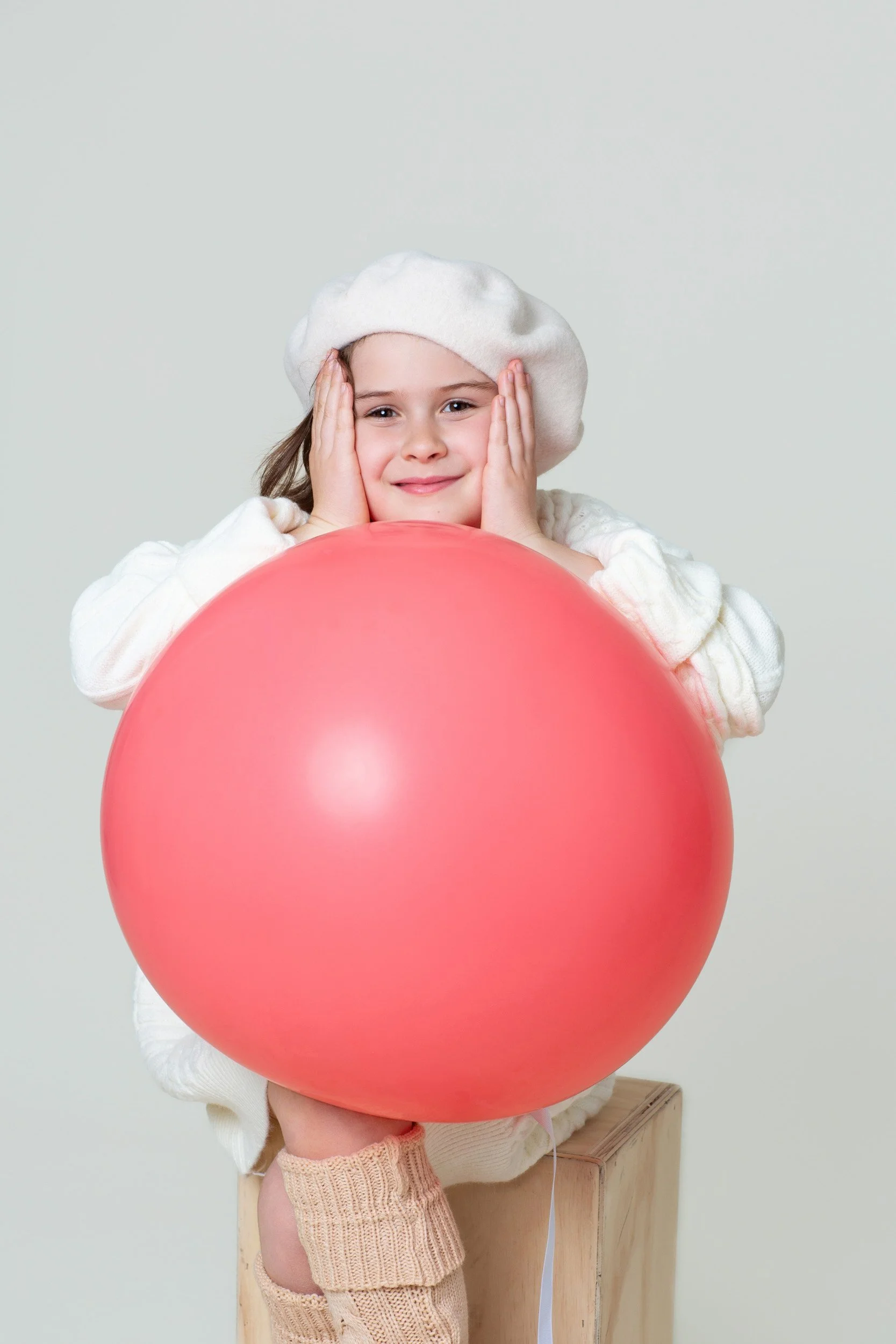 Girl in a white hat and cream outfit holding a large red balloon
