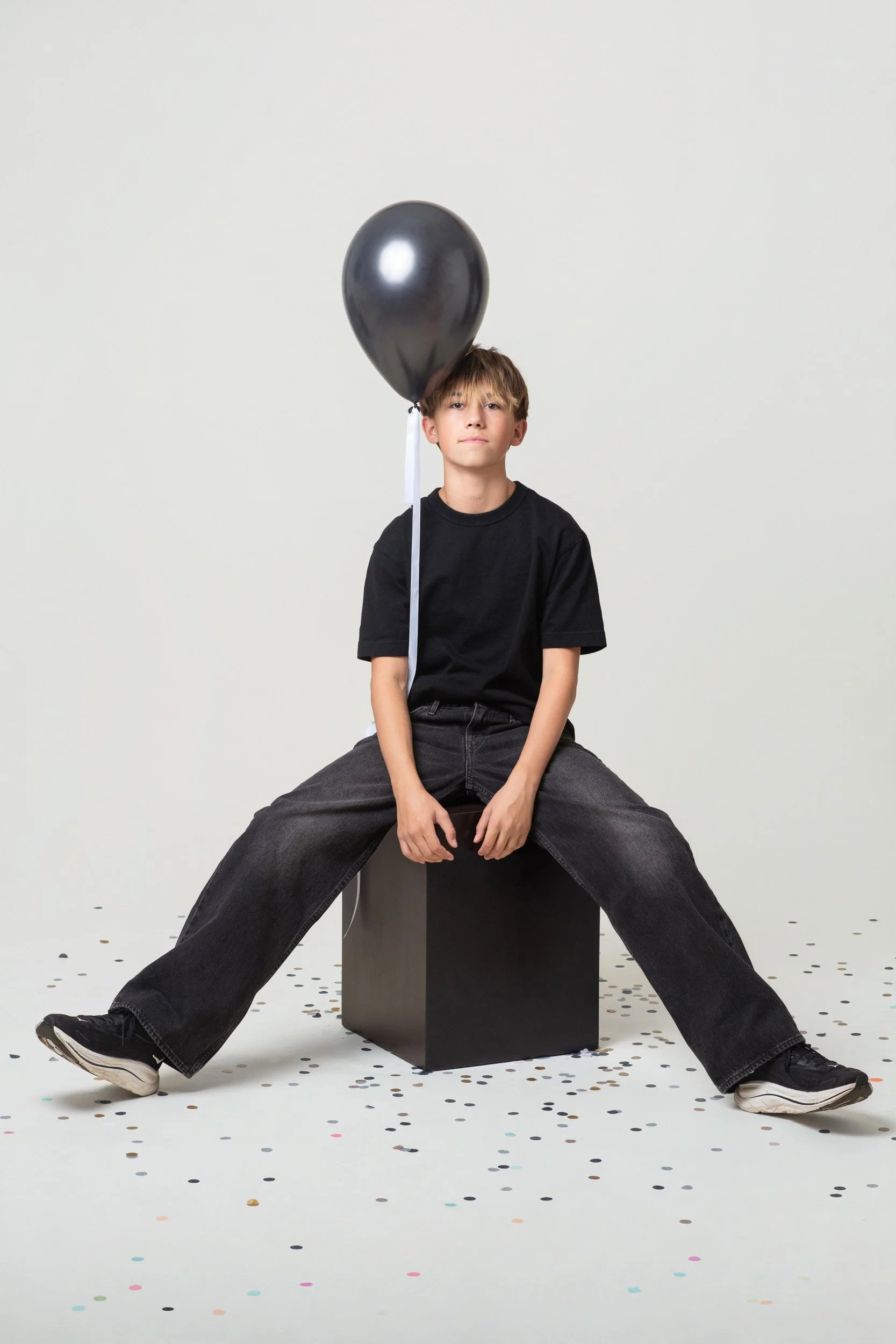 A boy sitting on a display cube with a single birthday balloon during a kids birthday portraits session at Poppie Portraits in Madrona, Seattle.  