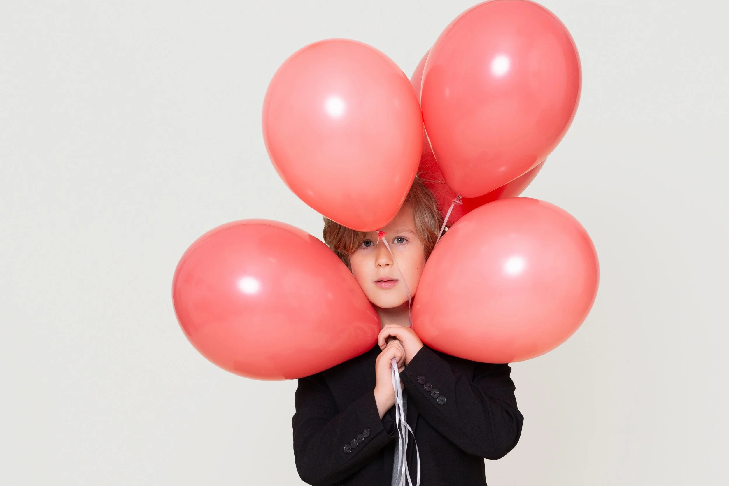 Child peeking through a cluster of red balloons during a birthday photoshoot at Poppie Portraits in Seattle.  