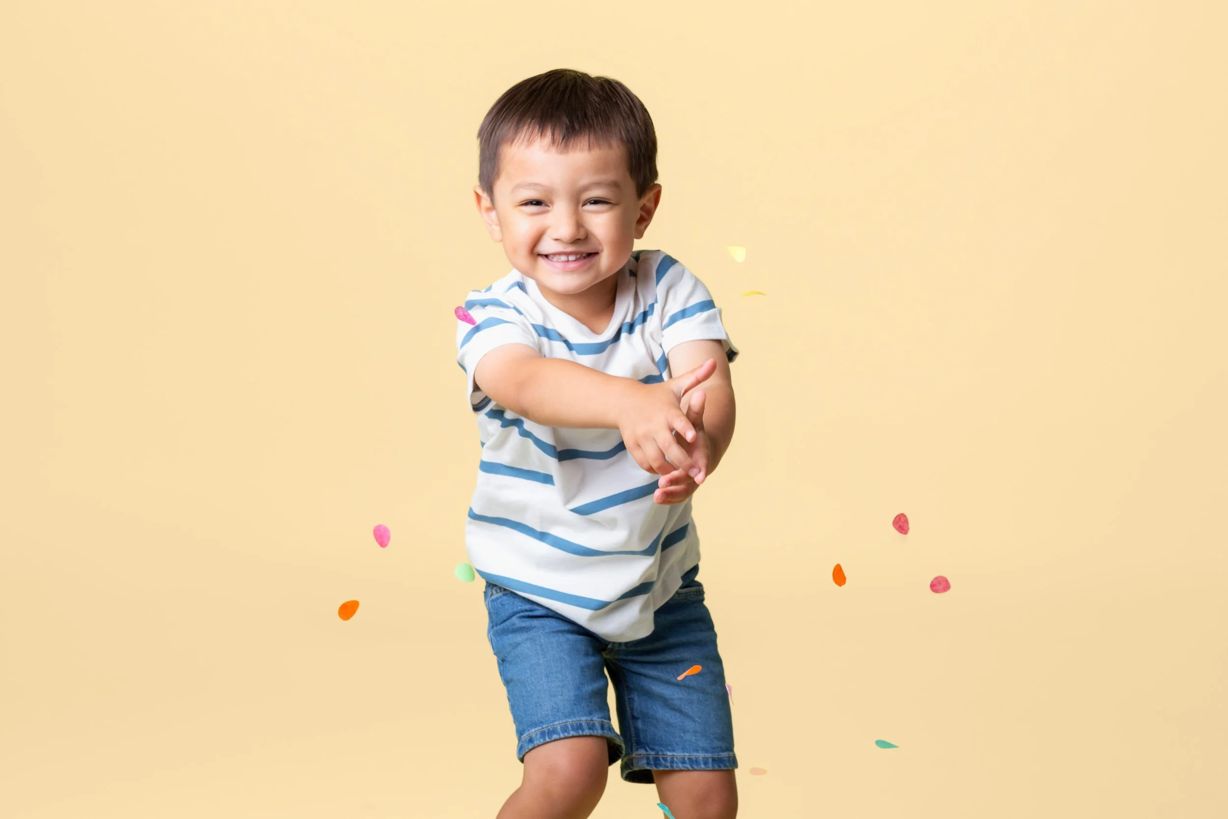 Smiling boy in a striped shirt against a yellow background with confetti in the air during a birthday photoshoot at Poppie Portraits in Seattle. 