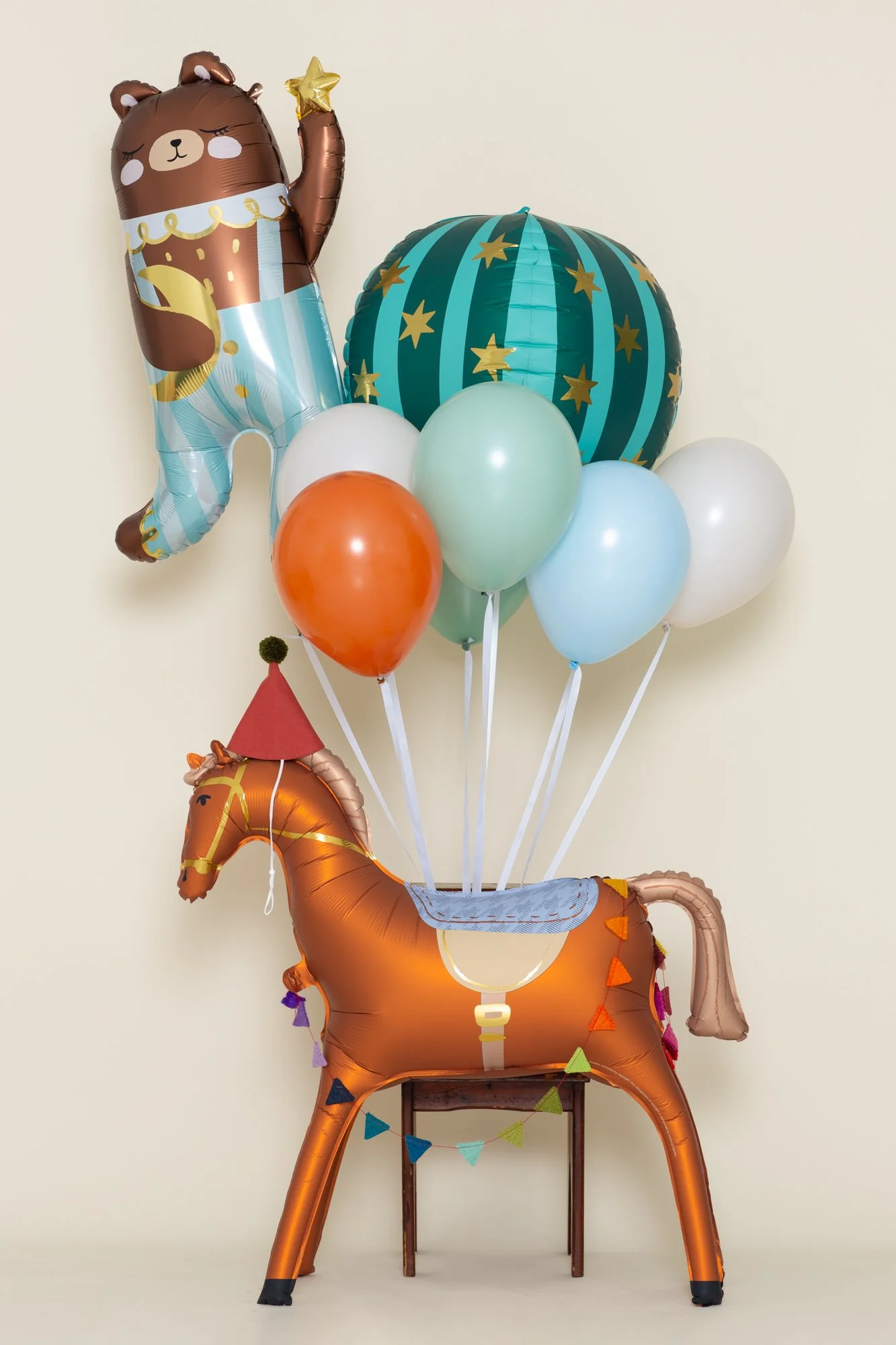 Circus-themed birthday balloon bouquet with an acrobat bear, a striped star ball, and a horse in a party hat.