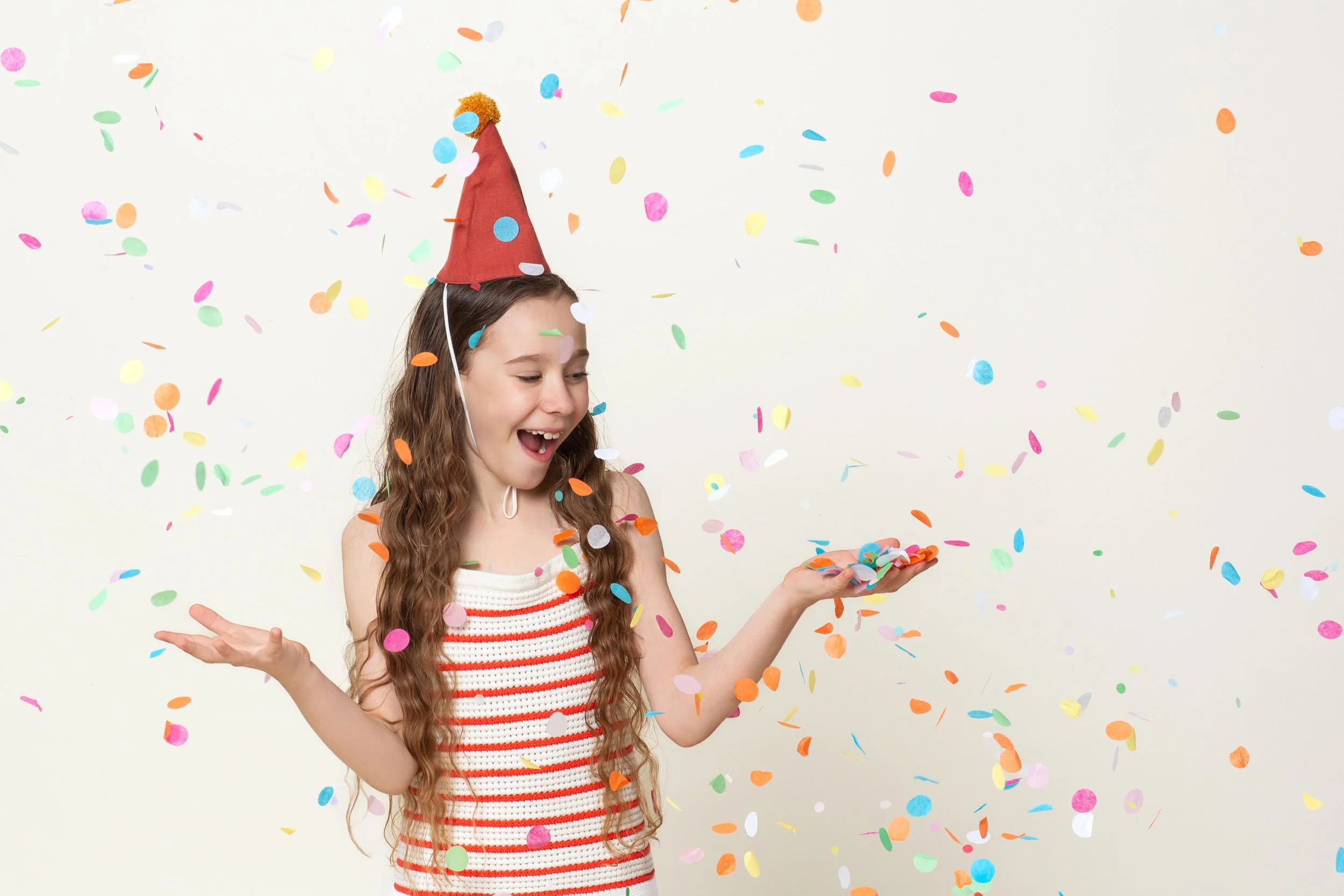 A happy girl in a party hat catching falling confetti during a kids birthday portraits session at Poppie Portraits in Madrona, Seattle.  