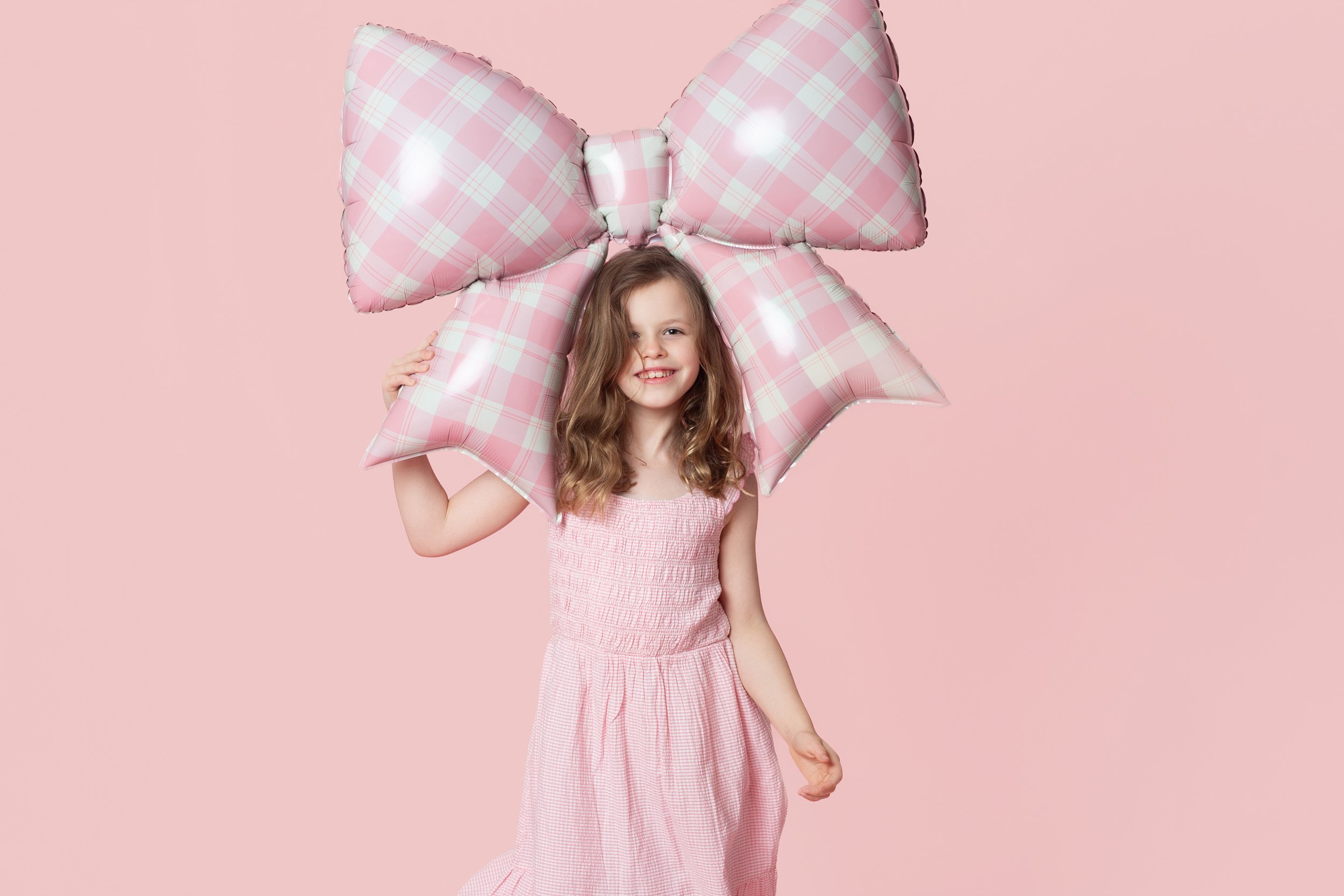 Girl holding a large pink gingham bow balloon in front of her