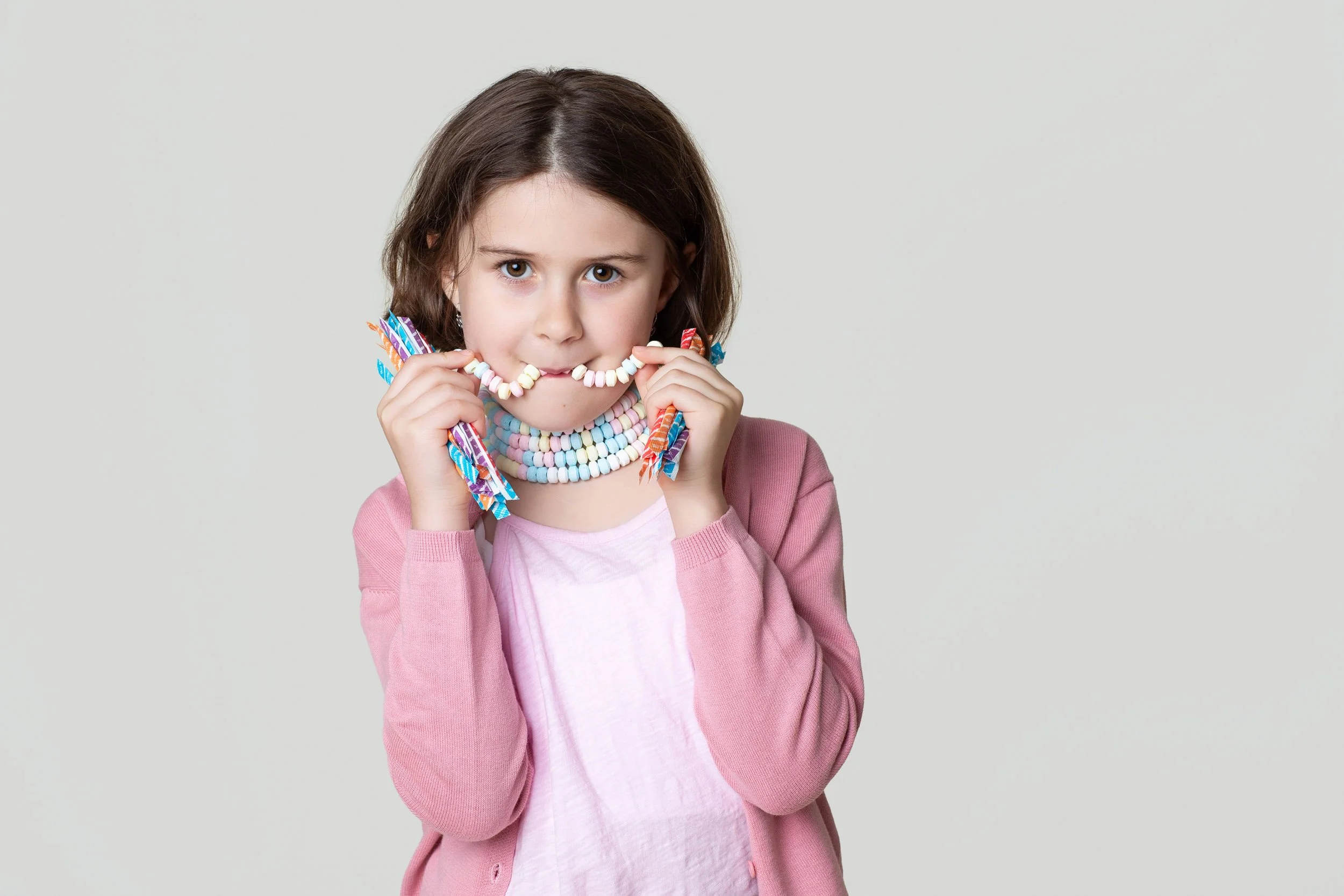 Girl in a pink cardigan biting into a candy necklace