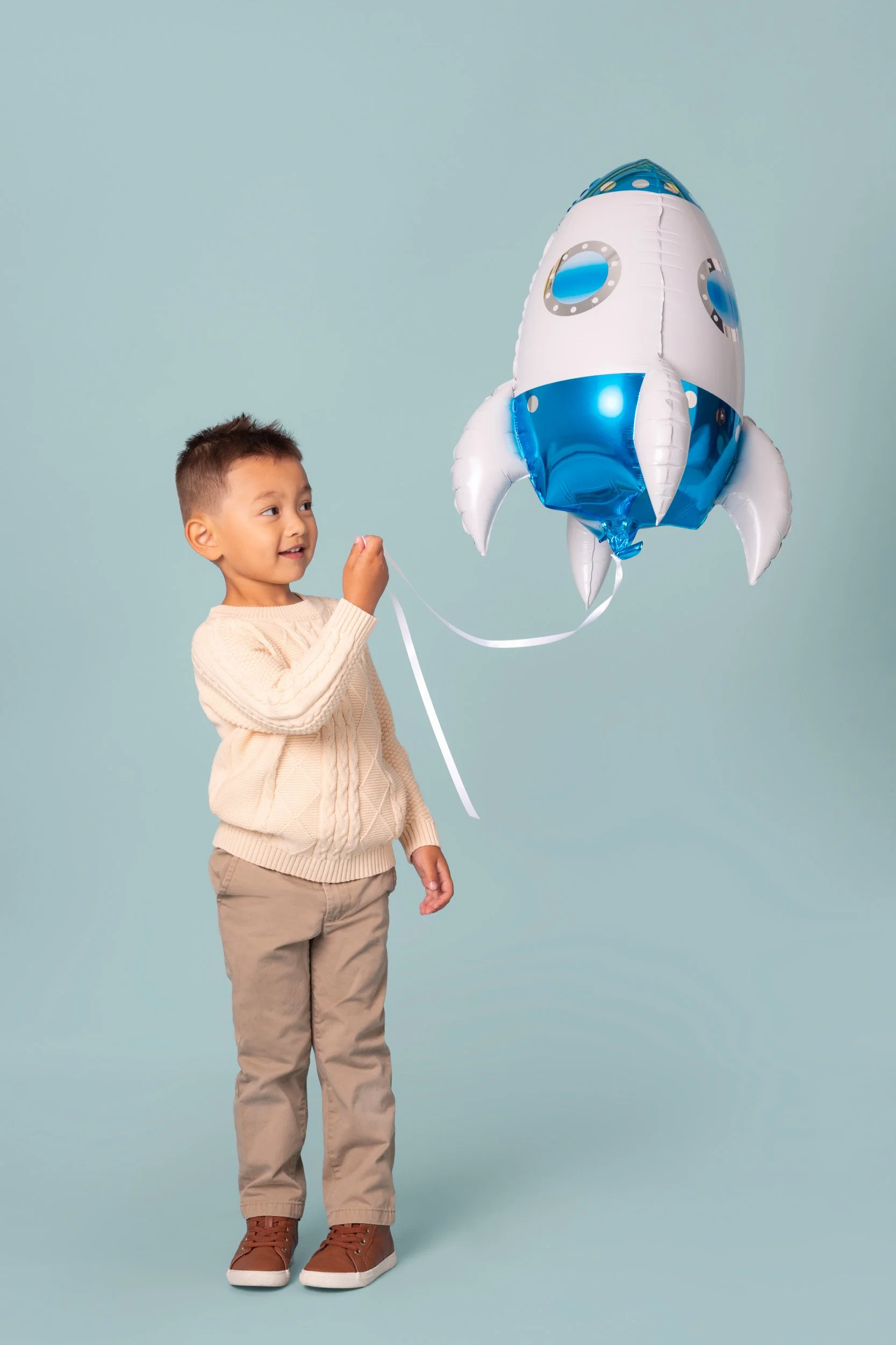 Boy with a lollipop holding a blue rocket foil balloon during a birthday photoshoot at Poppie Portraits in Seattle. 