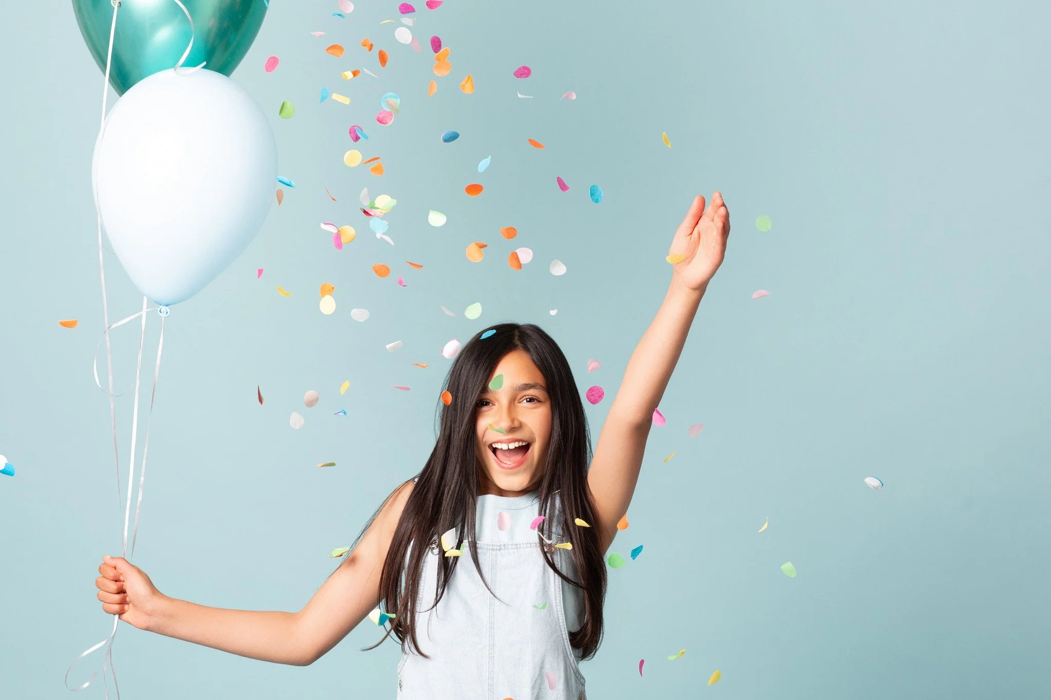 A joyful young girl throwing confetti next to a balloon bouquet during a kids birthday portraits session at Poppie Portraits in Seattle.