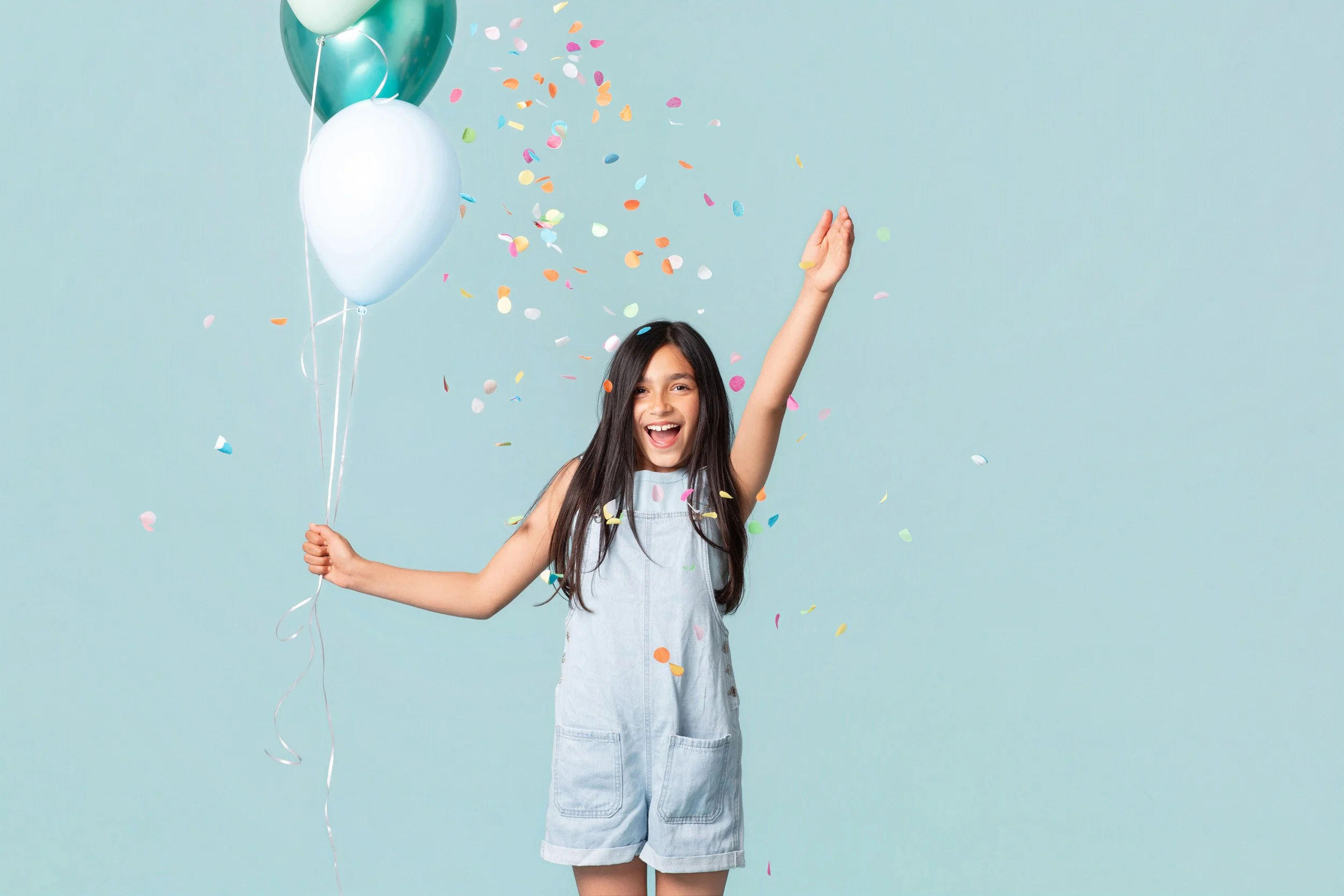 A joyful young girl throwing confetti next to a balloon bouquet during a kids birthday portraits session at Poppie Portraits in Seattle.