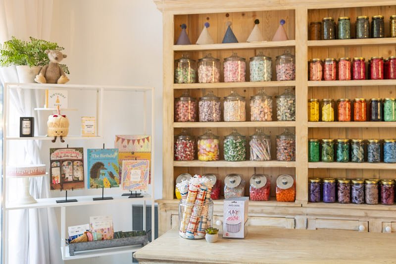Inside the Poppie birthday boutique and candy shop in Madrona, Seattle, featuring rows of custom balloon color bar jars and gift displays.