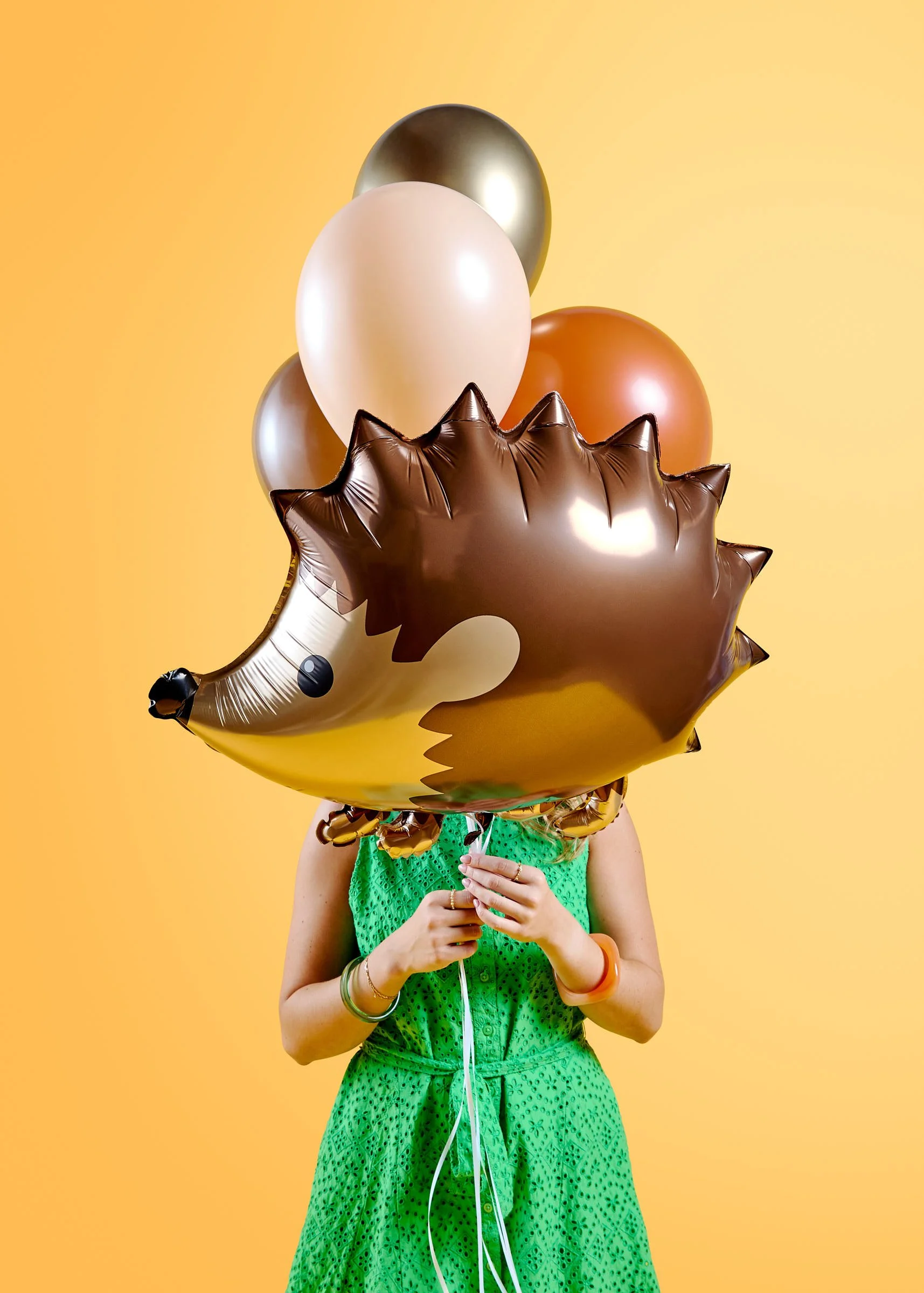 A young girl holding a whimsical hedgehog statement balloon over her face for a birthday photoshoot at Poppie Portraits in Seattle.