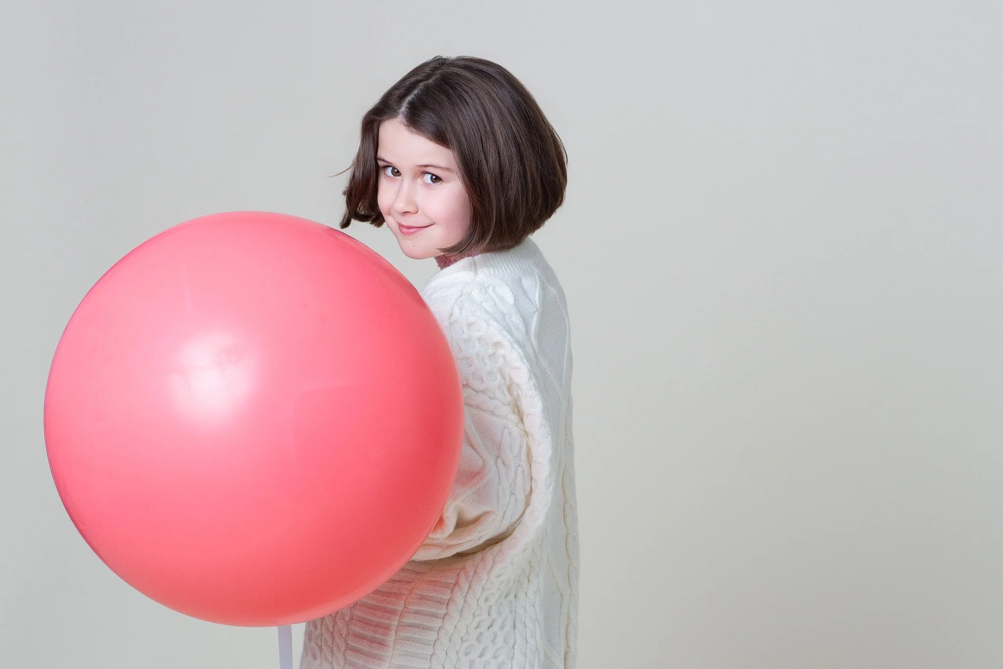 Profile view of a smiling girl holding a large pink balloon during a kids birthday portraits session at Poppie Portraits in Madrona, Seattle.  