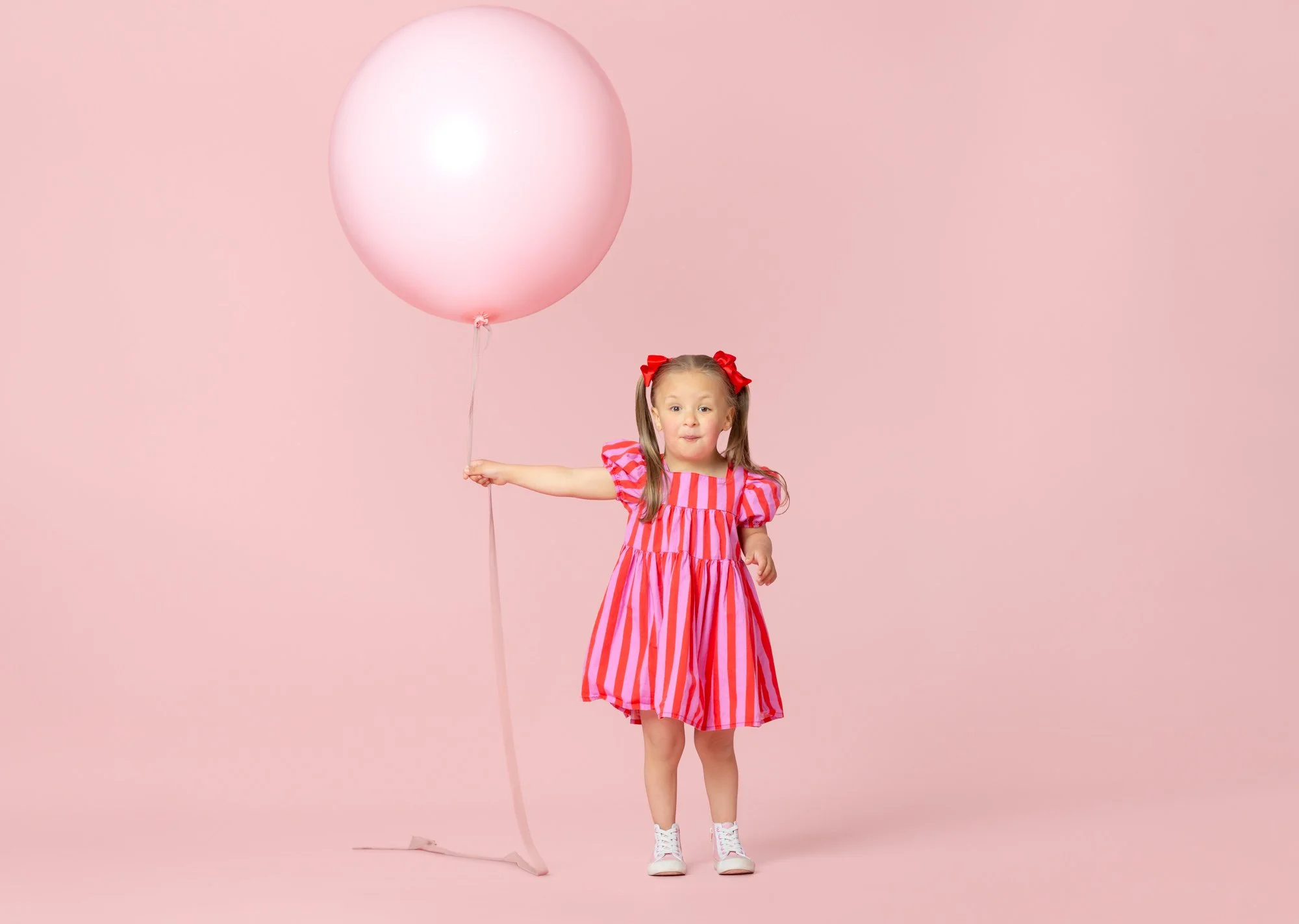 Young girl in a pink dress walking with a pink balloon on a long string