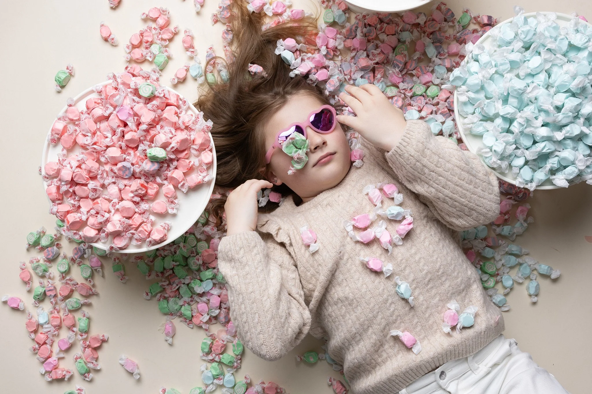 Overhead portrait of a young girl lying down among old-fashioned candy counter treats during a playful milestone birthday photos session at Poppie Portraits in Seattle.  