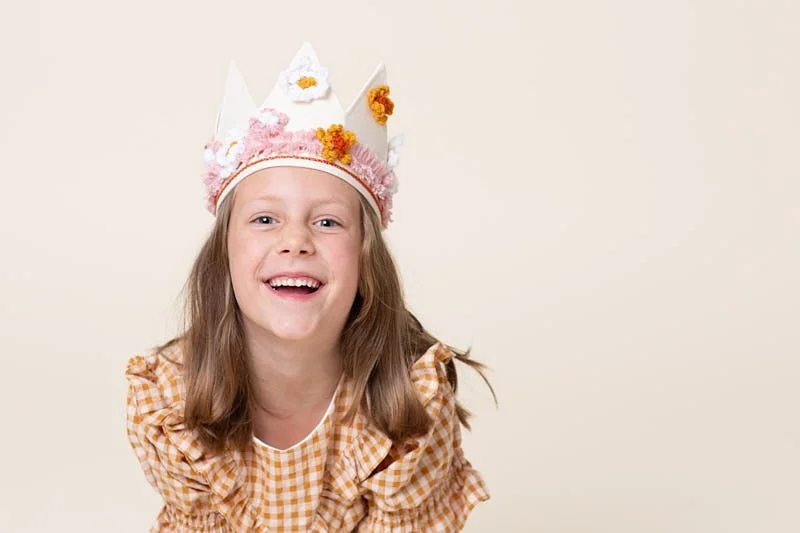 A young girl laughing in a handcrafted floral party crown during a kids birthday portraits session at Poppie Portraits in Madrona, Seattle.