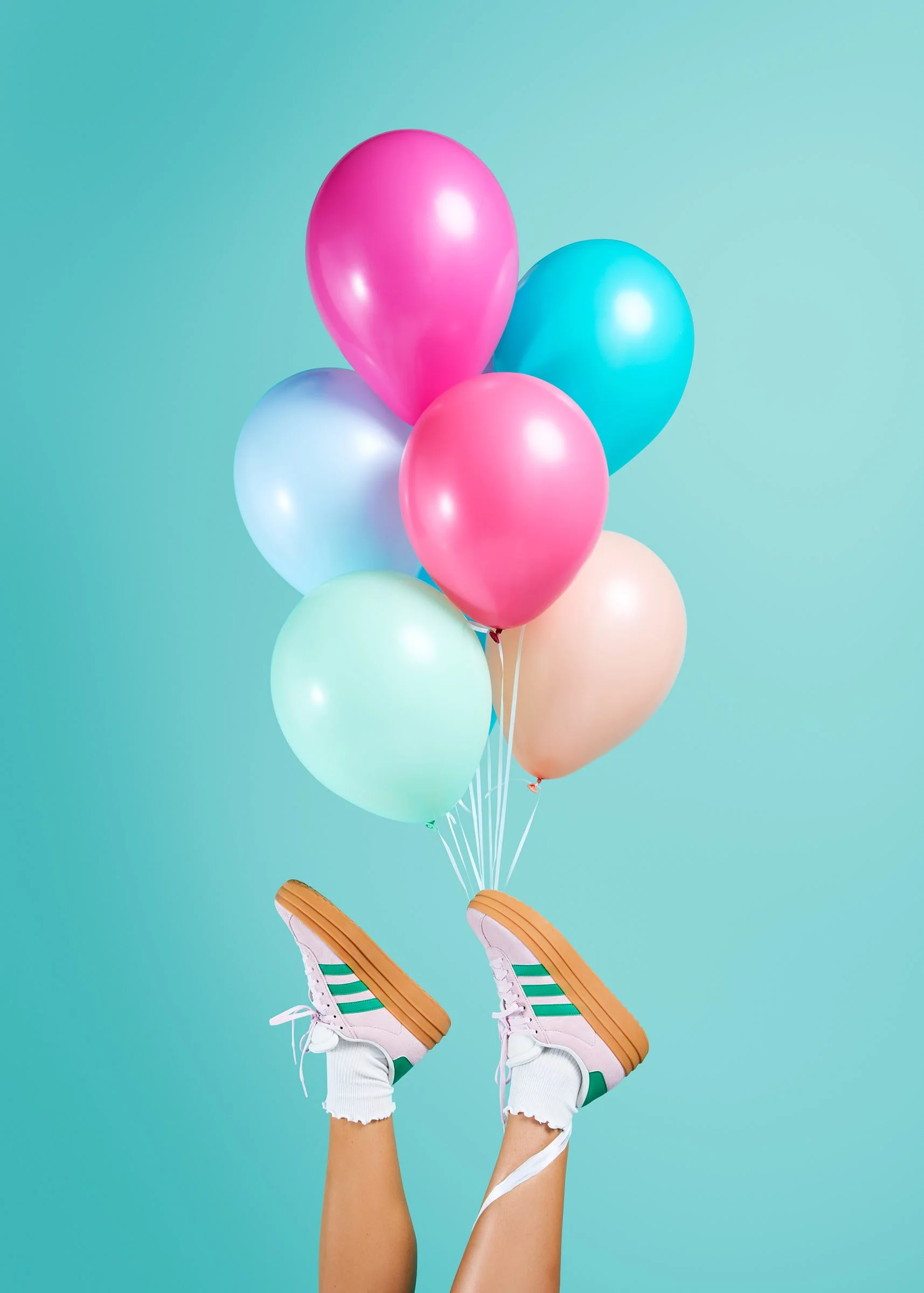 A colorful balloon bouquet featuring bright pink, blue, mint, and peach latex balloons tied to pink sneakers against a teal background at Poppie in Madrona, Seattle.
