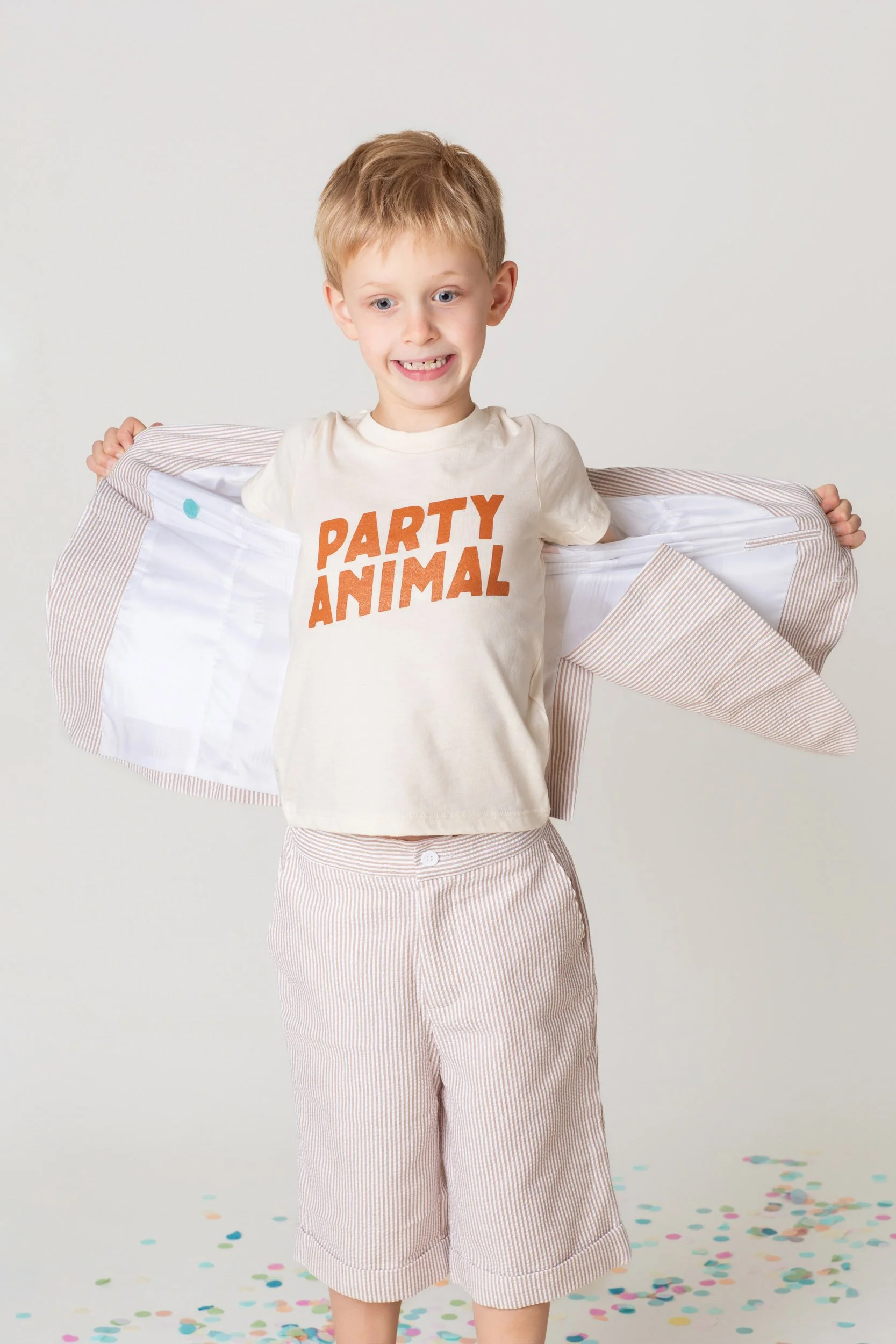 Boy in a Party Animal shirt stretching a paper streamer between his hands during a birthday photoshoot at Poppie Portraits in Seattle. 