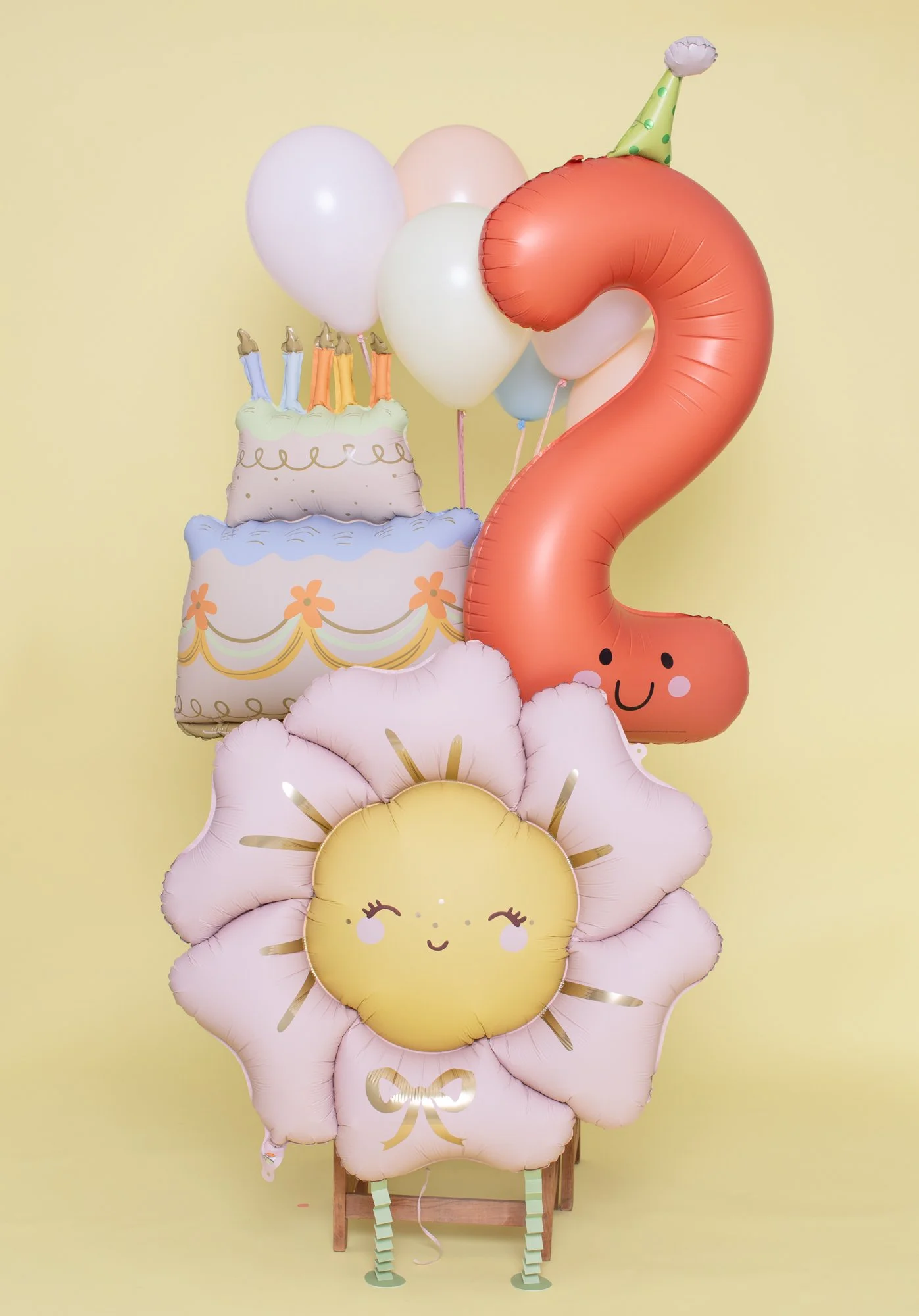 Second birthday balloon bouquet with a smiling coral number 2, layer cake balloon, and blush daisy on pale yellow.