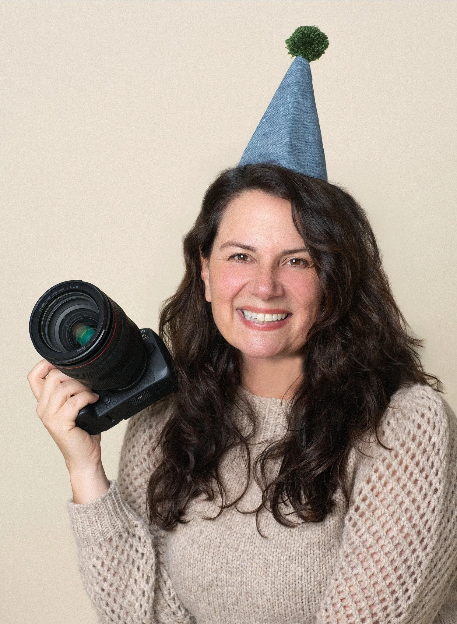 Photographer Christina holding her camera and wearing a party hat at Poppie Portraits, a premier kids birthday photo studio in Madrona, Seattle.
