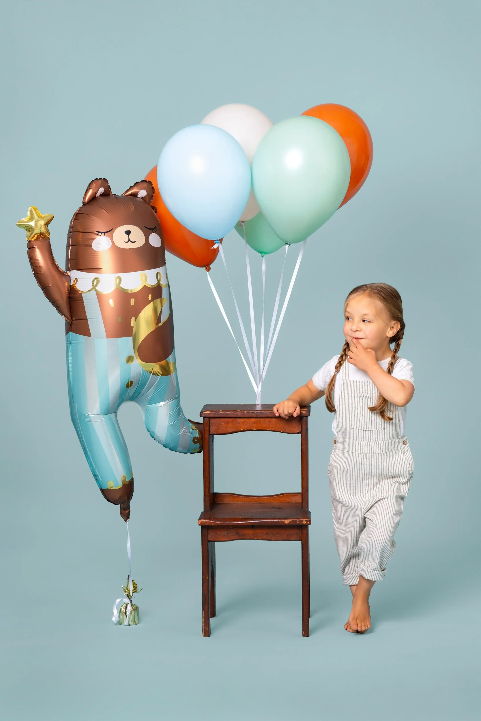Girl in white standing beside a tall bear foil balloon and a balloon bunch during a birthday photoshoot at Poppie Portraits in Seattle. 