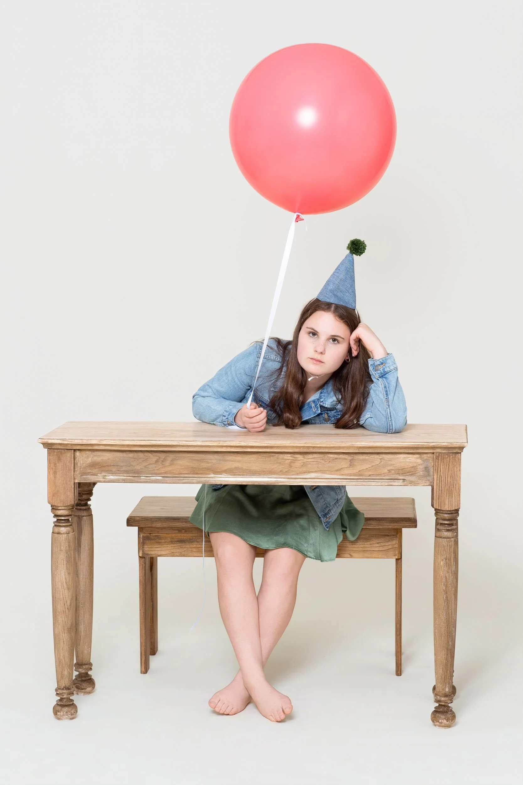 Girl resting at a wooden table with a red balloon floating above her