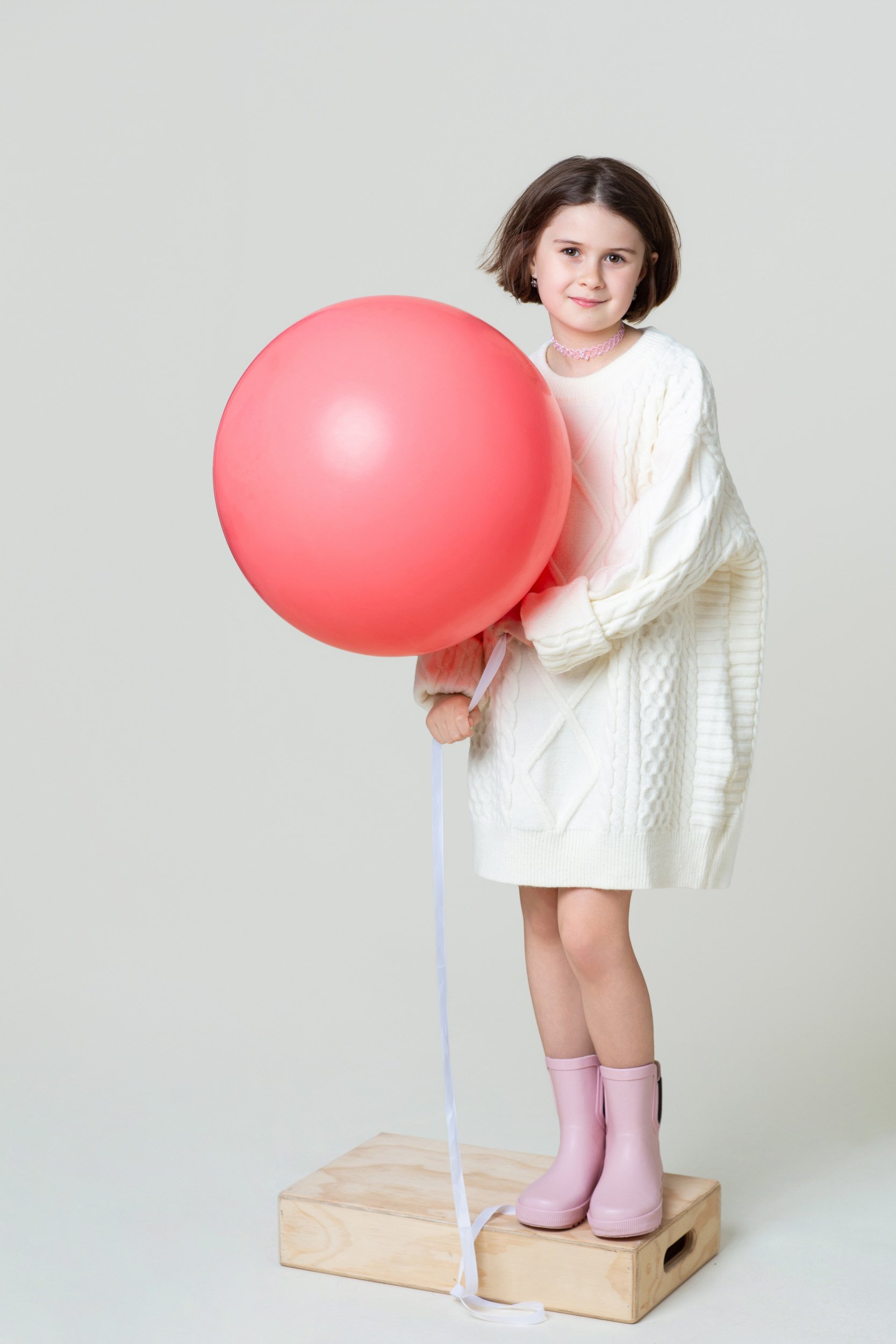 Girl in a white dress standing on a wooden block with a red balloon