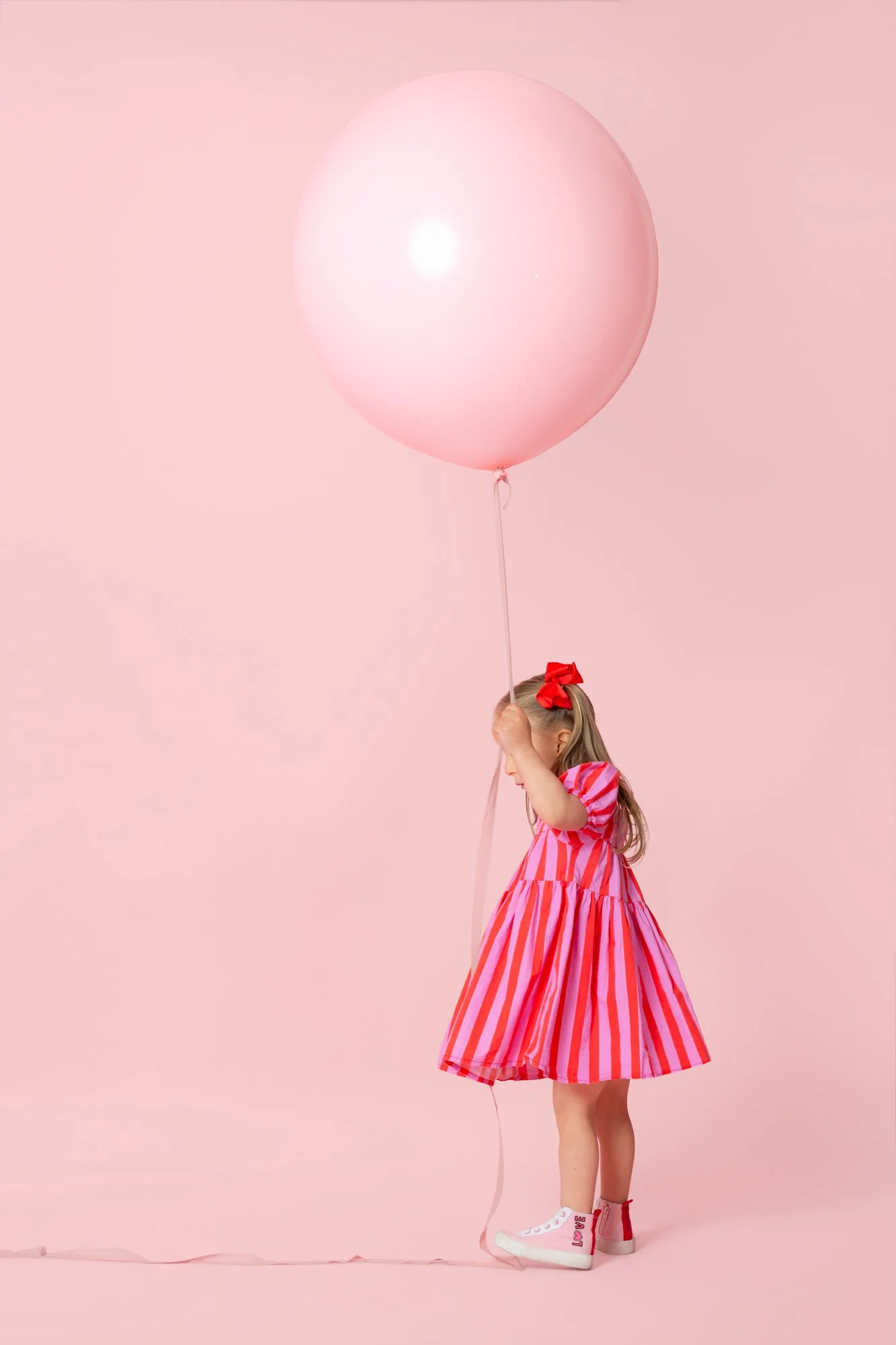 Girl in a pink dress holding a pink balloon on a pink background