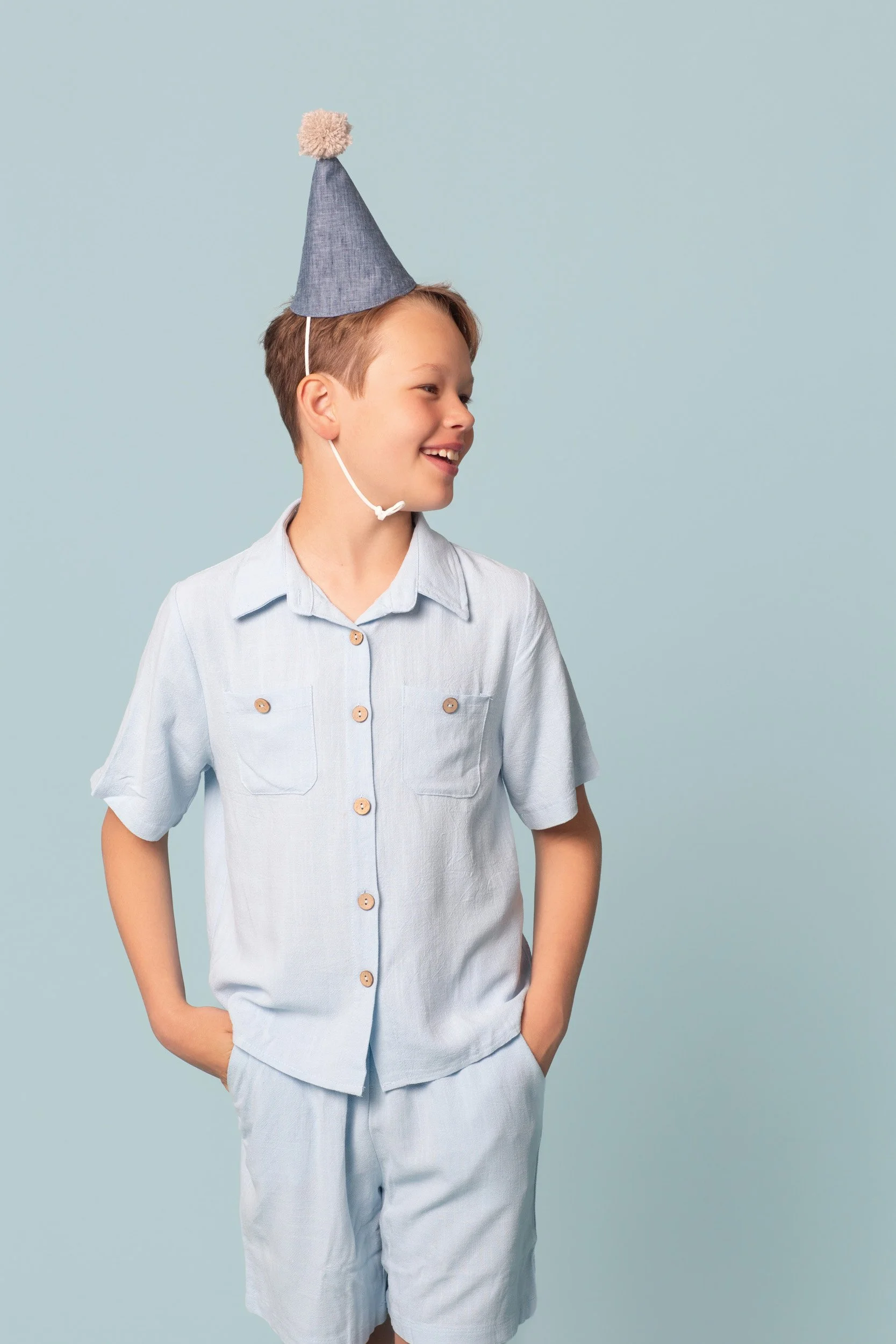 A smiling boy wearing a party hat against an aqua background tint during a kids birthday portraits session at Poppie Portraits in Madrona, Seattle.  