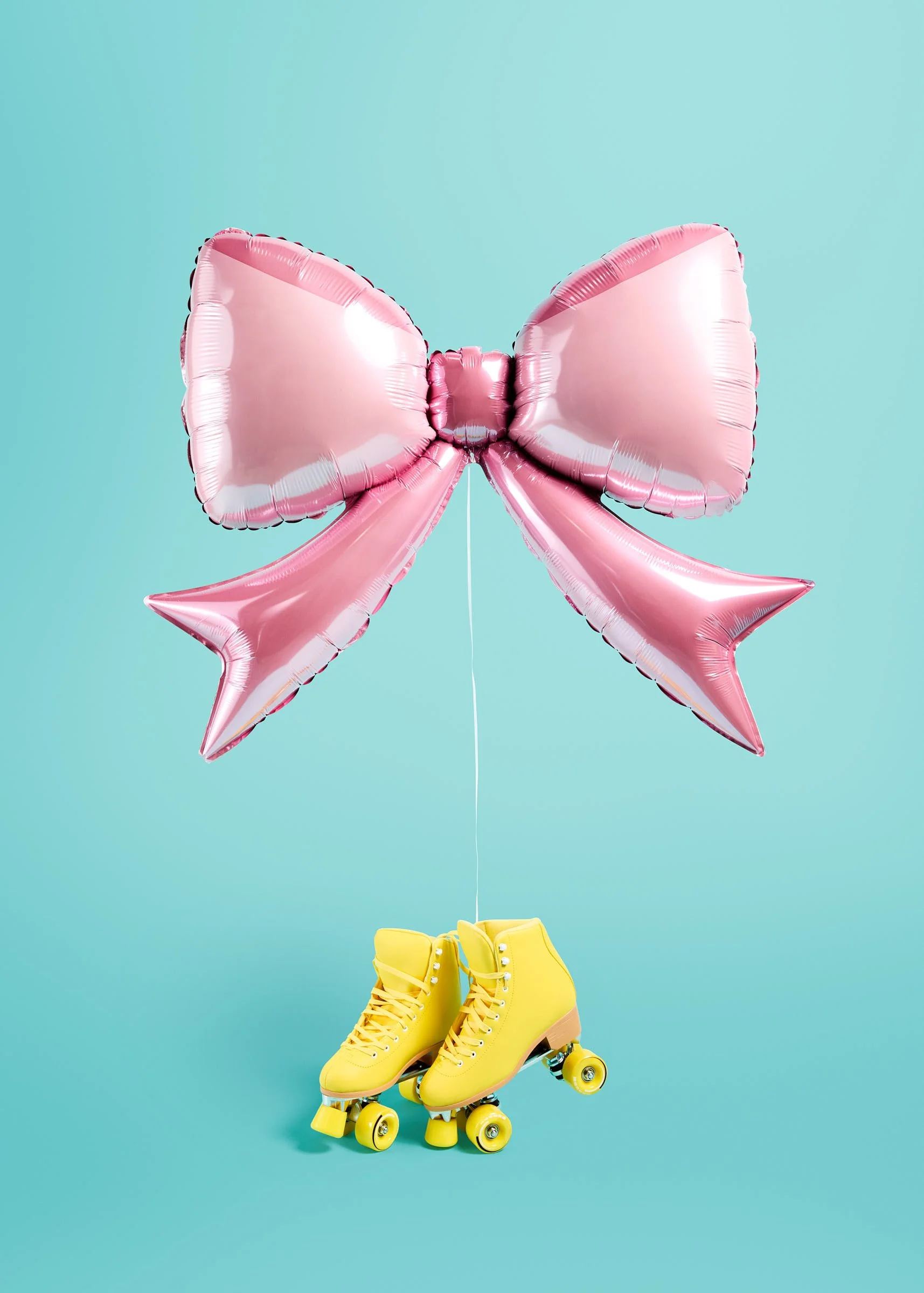 A metallic pink bow balloon styled with yellow roller skates against a bright teal backdrop at the Poppie balloon boutique in Madrona, Seattle.