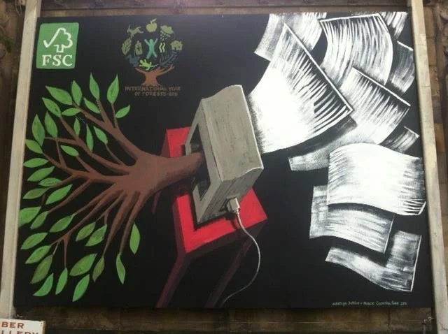 Chalkboard art showing a tree with green leaves connected to sheets of paper by a large paper hole punch, symbolizing environmental awareness and paper recycling, with FSC certification logo in the top left corner.