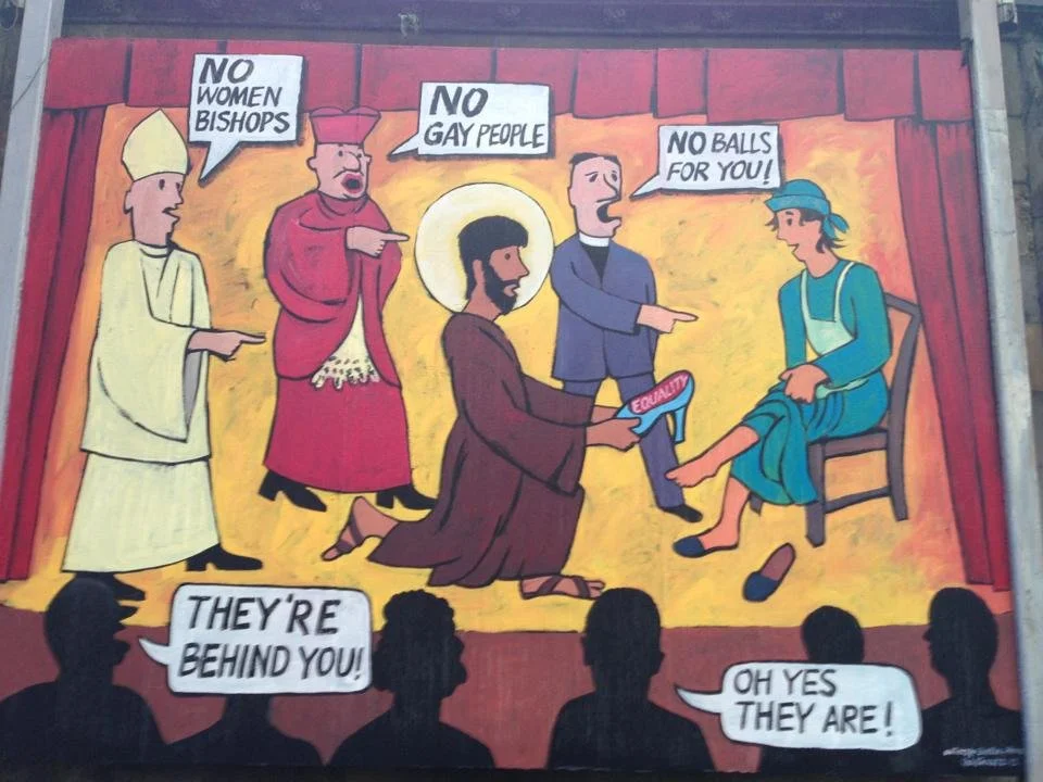 A humorous, cartoon-style mural depicts a parody of the nativity scene, with modern characters speaking politically charged lines about gender and sexuality. It features a man dressed as Jesus, with a halo, kneeling and holding a sign that says 'Equa