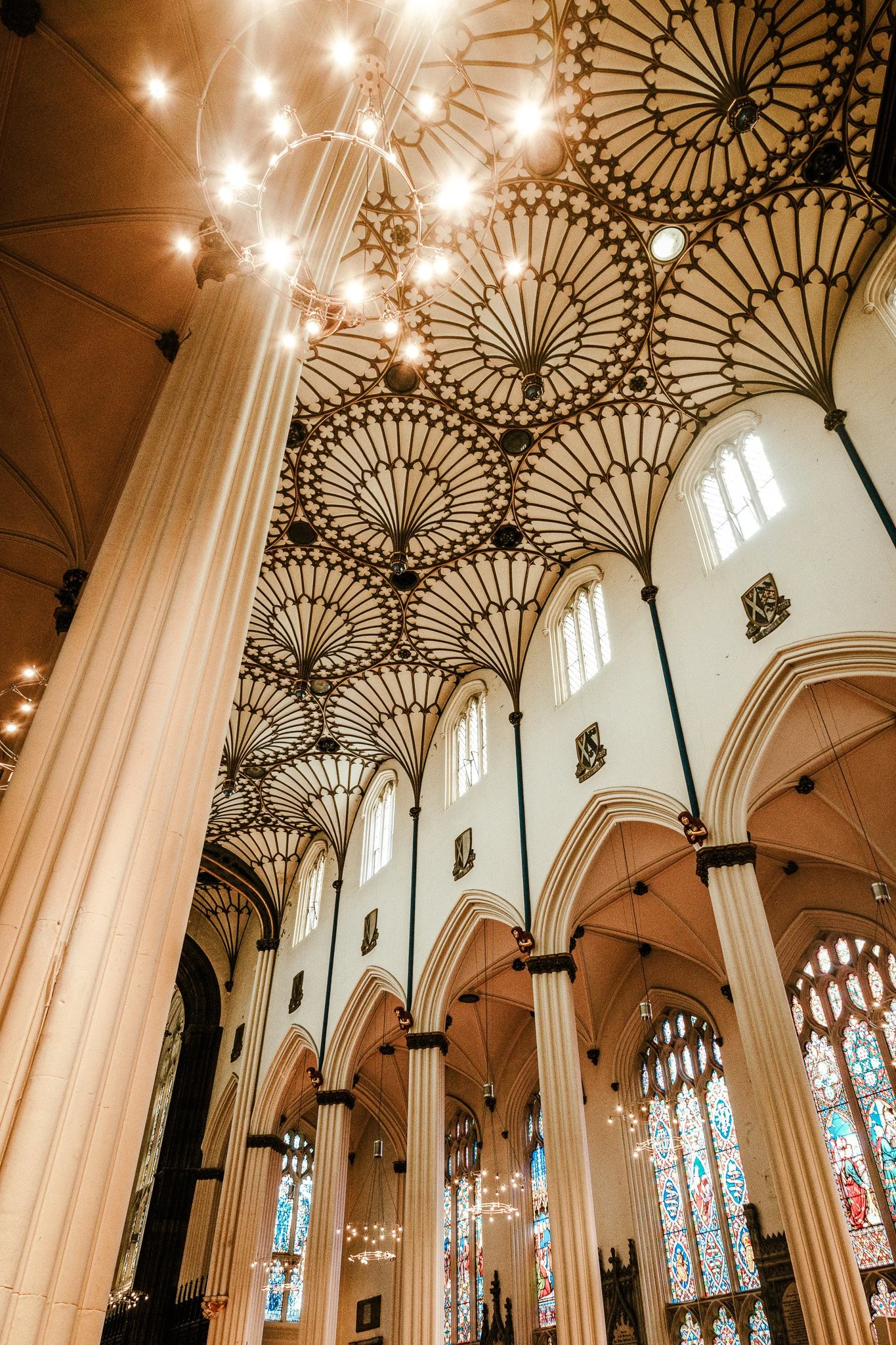 Interior view of a large church with tall white columns, stained glass windows, ornate ceiling patterns, and modern circular chandeliers hanging from the ceiling.