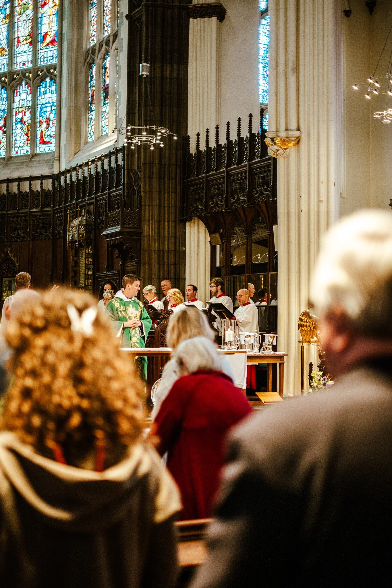 People gathered in a church for a service or ceremony, with stained glass windows and ornate woodwork in the background.