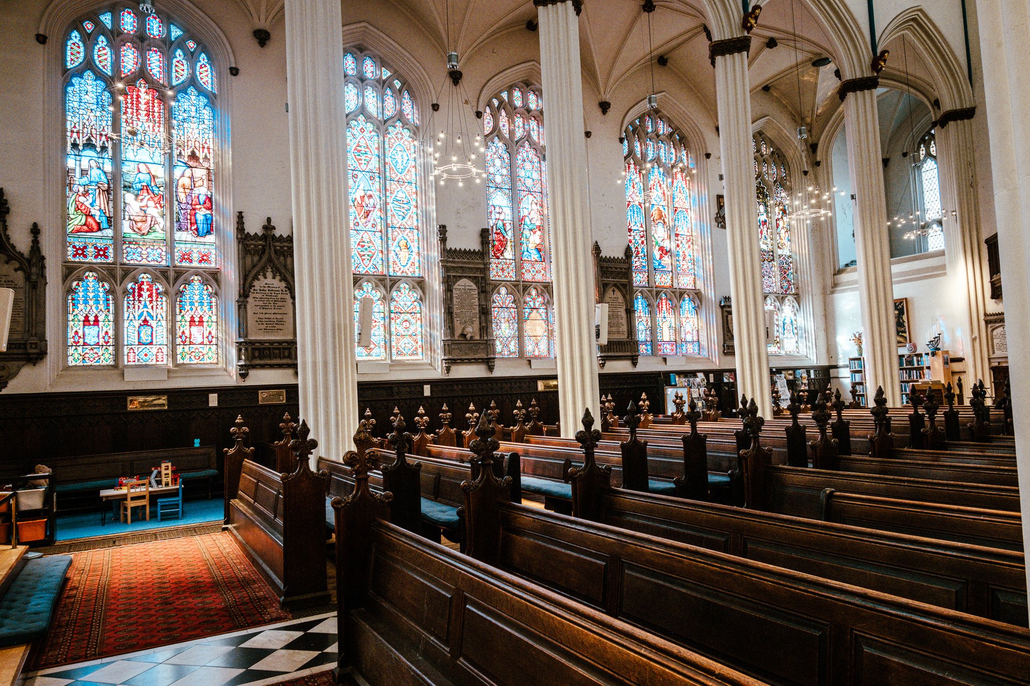 Interior of a church with large stained glass windows depicting religious scenes, wooden pews, and tall columns.
