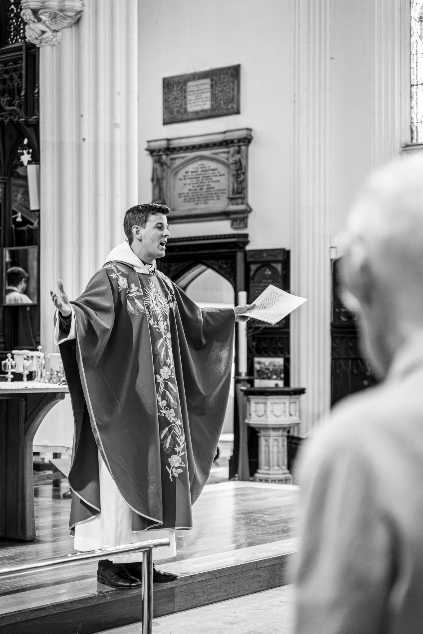 A priest in robes speaking in a church or chapel.