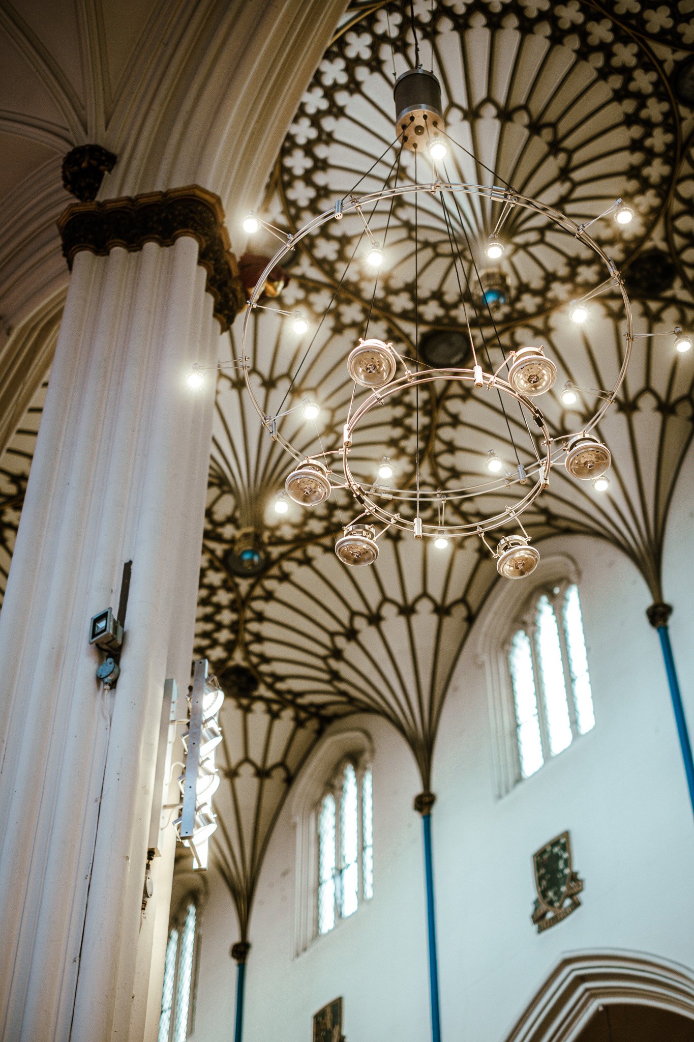 Inside view of a church with tall stained glass windows, ornate ceiling with gothic patterns, and a large modern chandelier with multiple lights hanging from the ceiling.