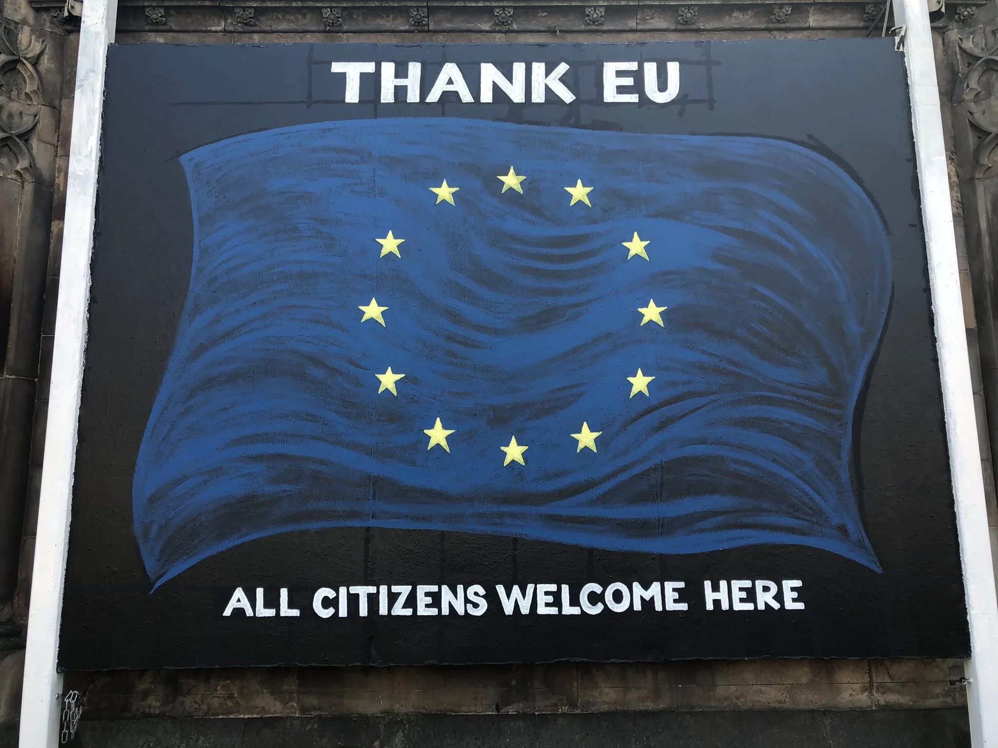 Chalkboard sign with blue and yellow EU flag design, with white text that reads, 'THANK EU' at the top and 'ALL CITIZENS WELCOME HERE' at the bottom.