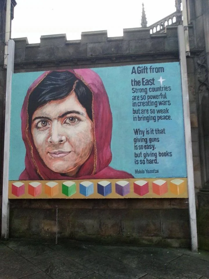 A mural featuring a woman with short dark hair wearing a pink headscarf, with a quote by Malala Yousafzai about the power of strong countries and the difficulty of giving books.